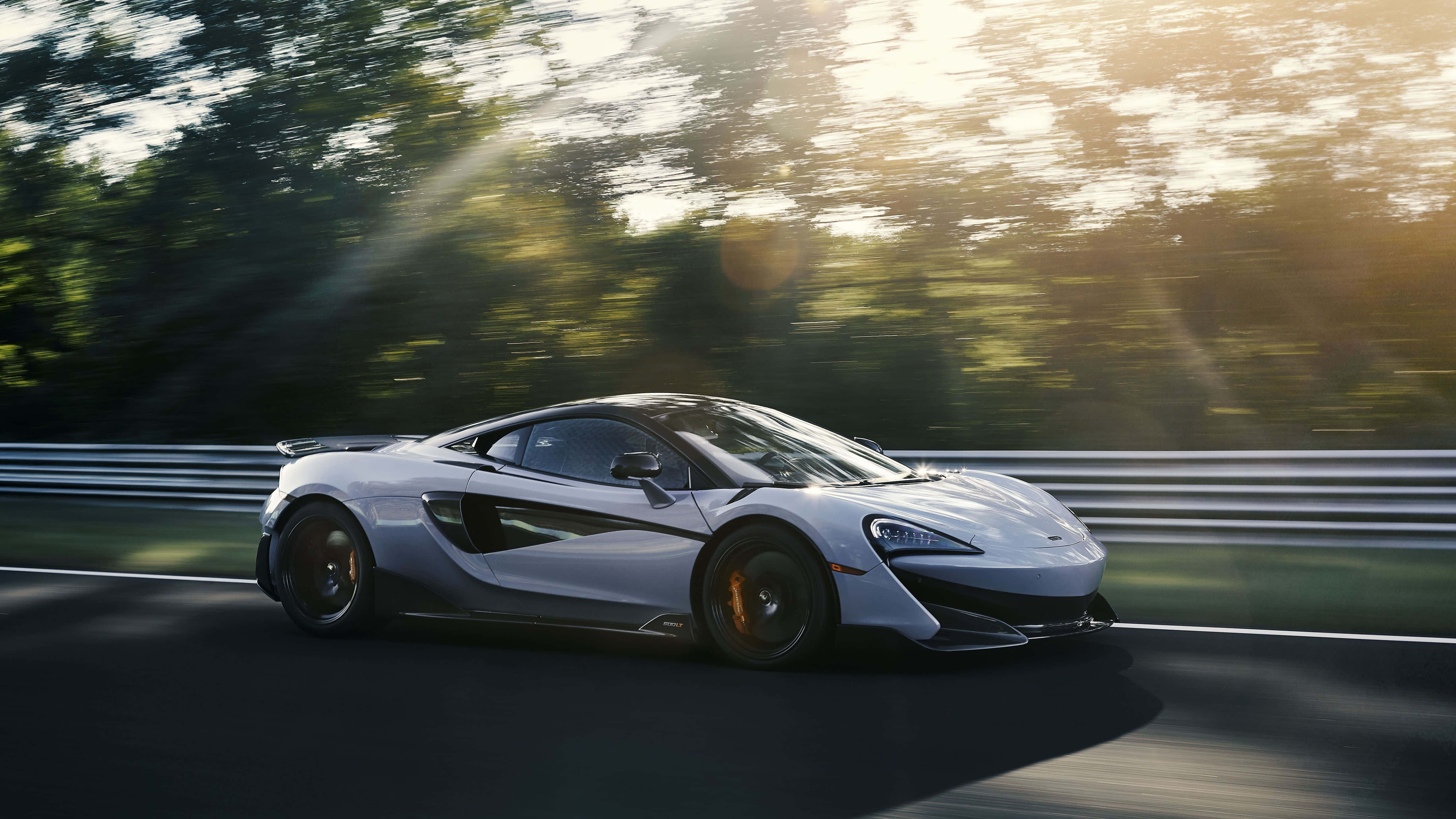 Mclaren 600lt 桌布 壁紙 — 一輛時尚的銀色McLaren跑車沿著樹林環繞的賽道疾馳，金色陽光穿過樹林灑落。