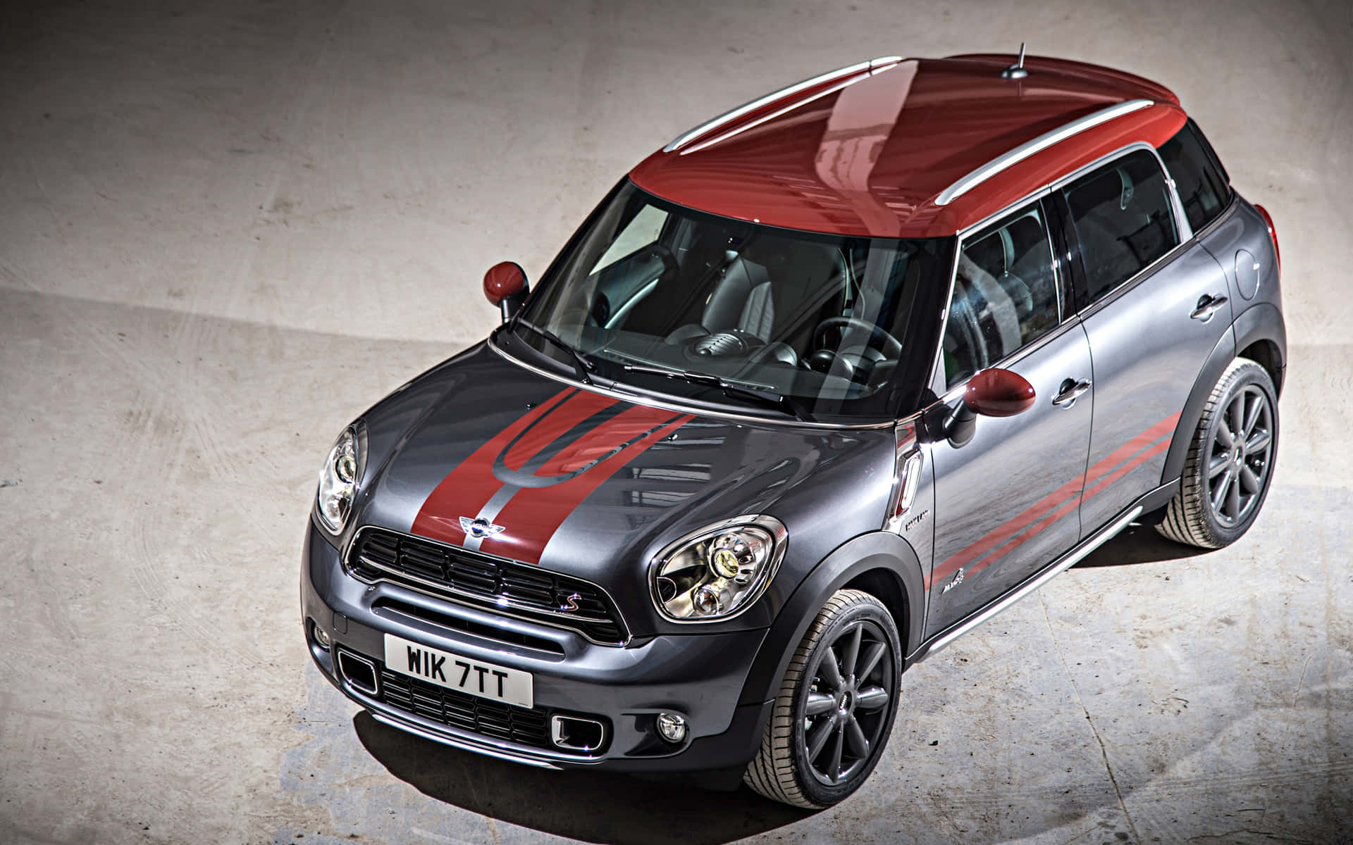  壁紙 — 一輛時尚的銀色MINI Countryman，紅色車頂和賽車條紋，停在混凝土車道上。