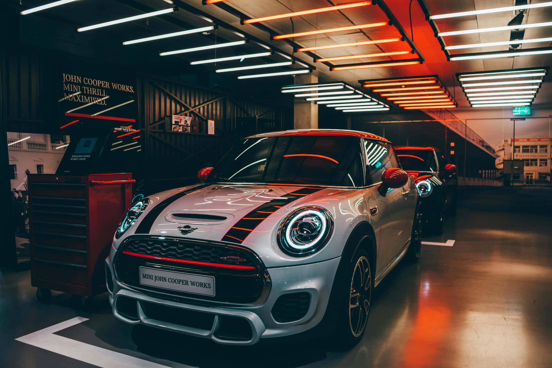  壁紙 — 一輛時尚的銀色MINI John Cooper Works汽車在現代車庫中，在鮮豔的橙色和白色霓虹燈下閃閃發光。