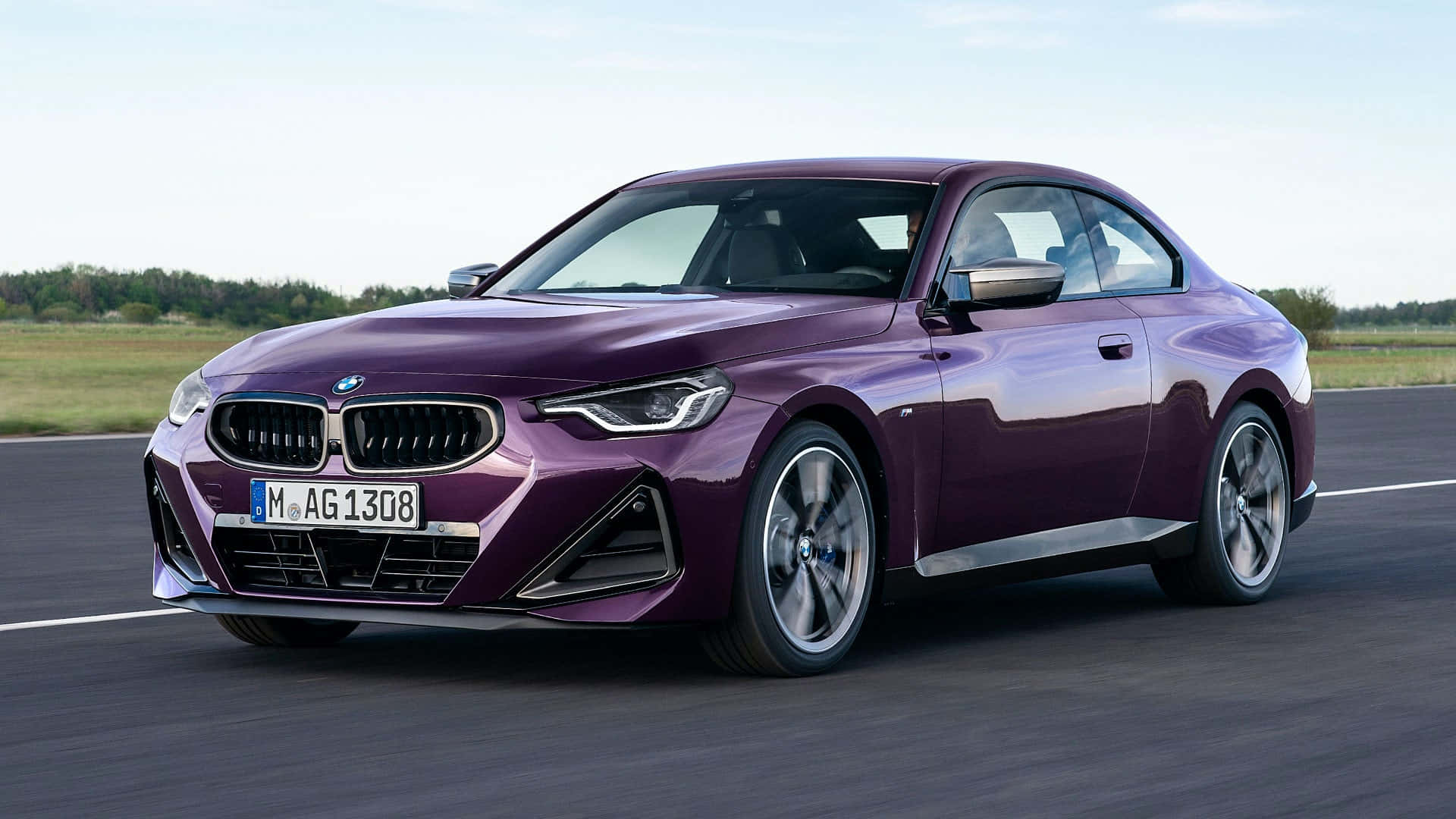 Bmw 2 Series 桌布 壁紙 — 一輛時尚的紫色寶馬轎跑車在晴朗的天空下，沿著開闊的道路奔馳，背景是草地田野。