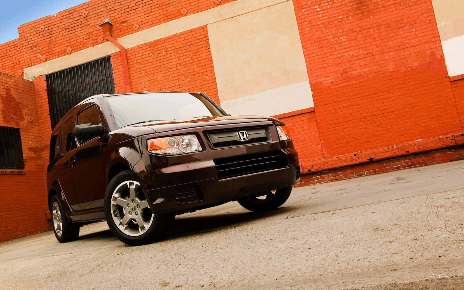 Honda Element 桌布 壁紙 — 一輛時尚的棕色本田Element以傾斜角度停放在鮮豔的紅磚牆前，天空清澈湛藍。