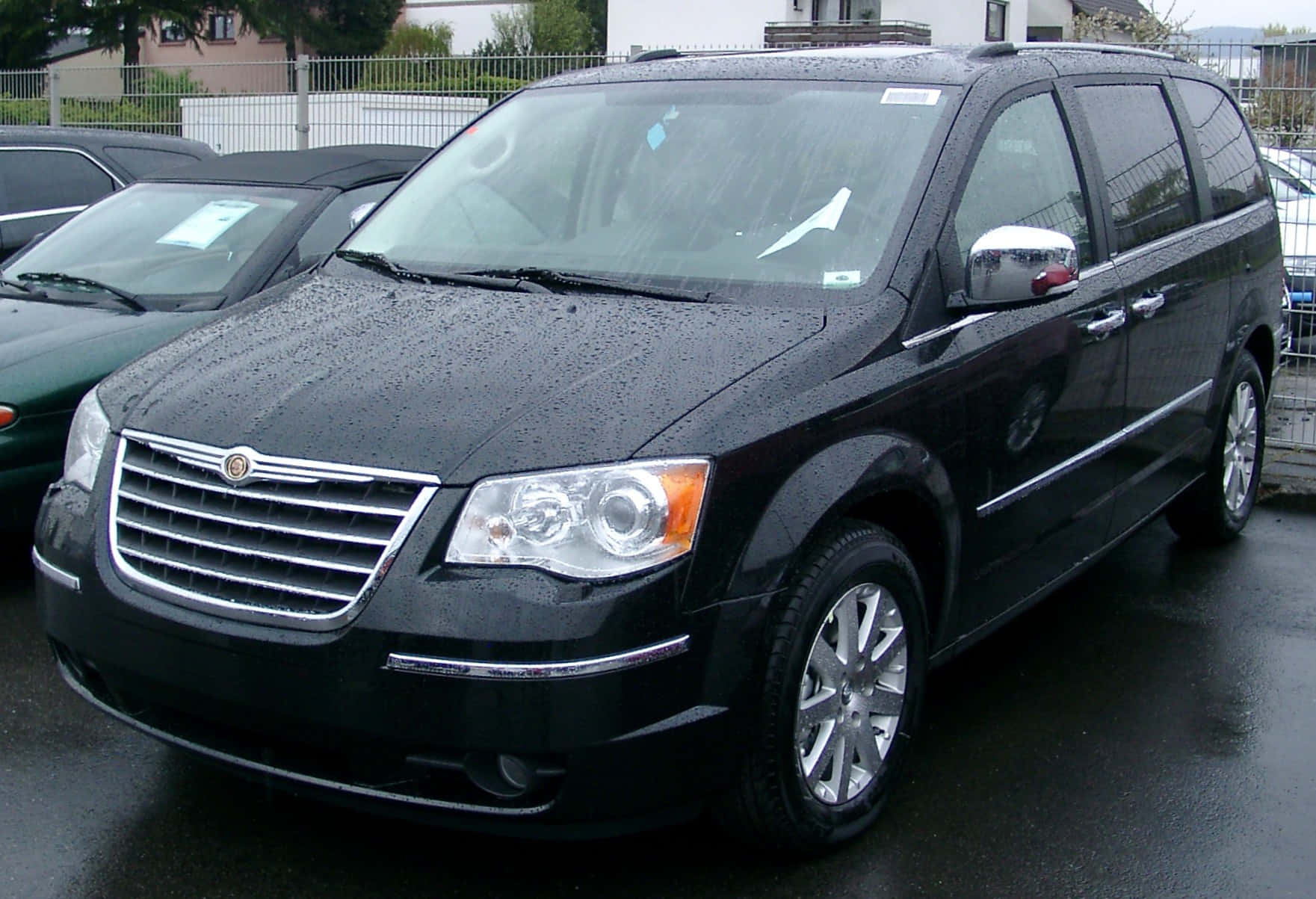 Chrysler Voyager 桌布 壁紙 — 一輛時尚的黑色克萊斯勒小型貨車在陰天停泊在濕漉漉的瀝青停車場上，閃爍著雨滴。