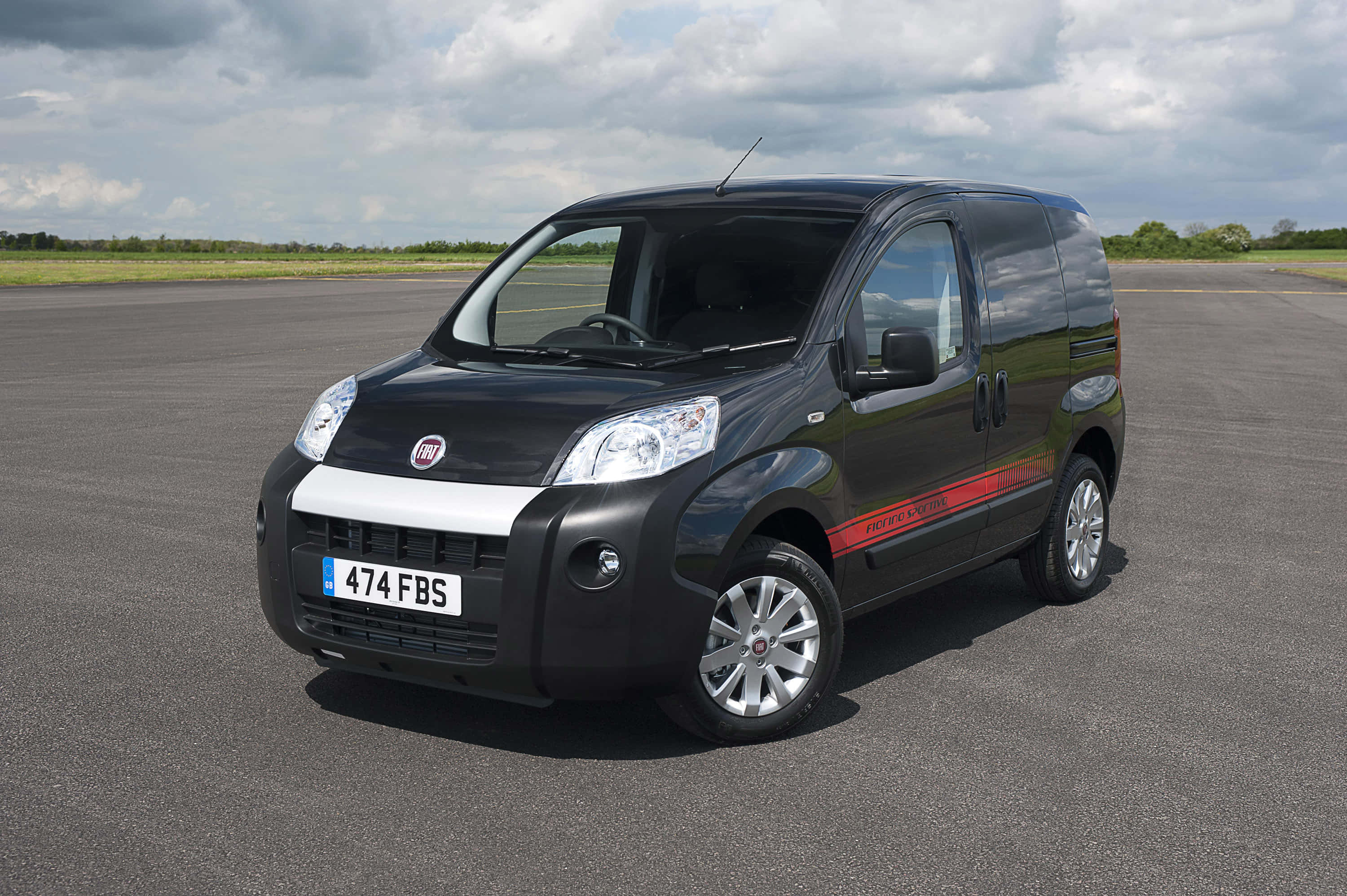 Fiat Fiorino 桌布 壁紙 — 一輛時尚黑色菲亞特 Fiorino 廂型車，帶有紅色賽車條紋，停泊在陰天下一條寬闊的瀝青跑道上。