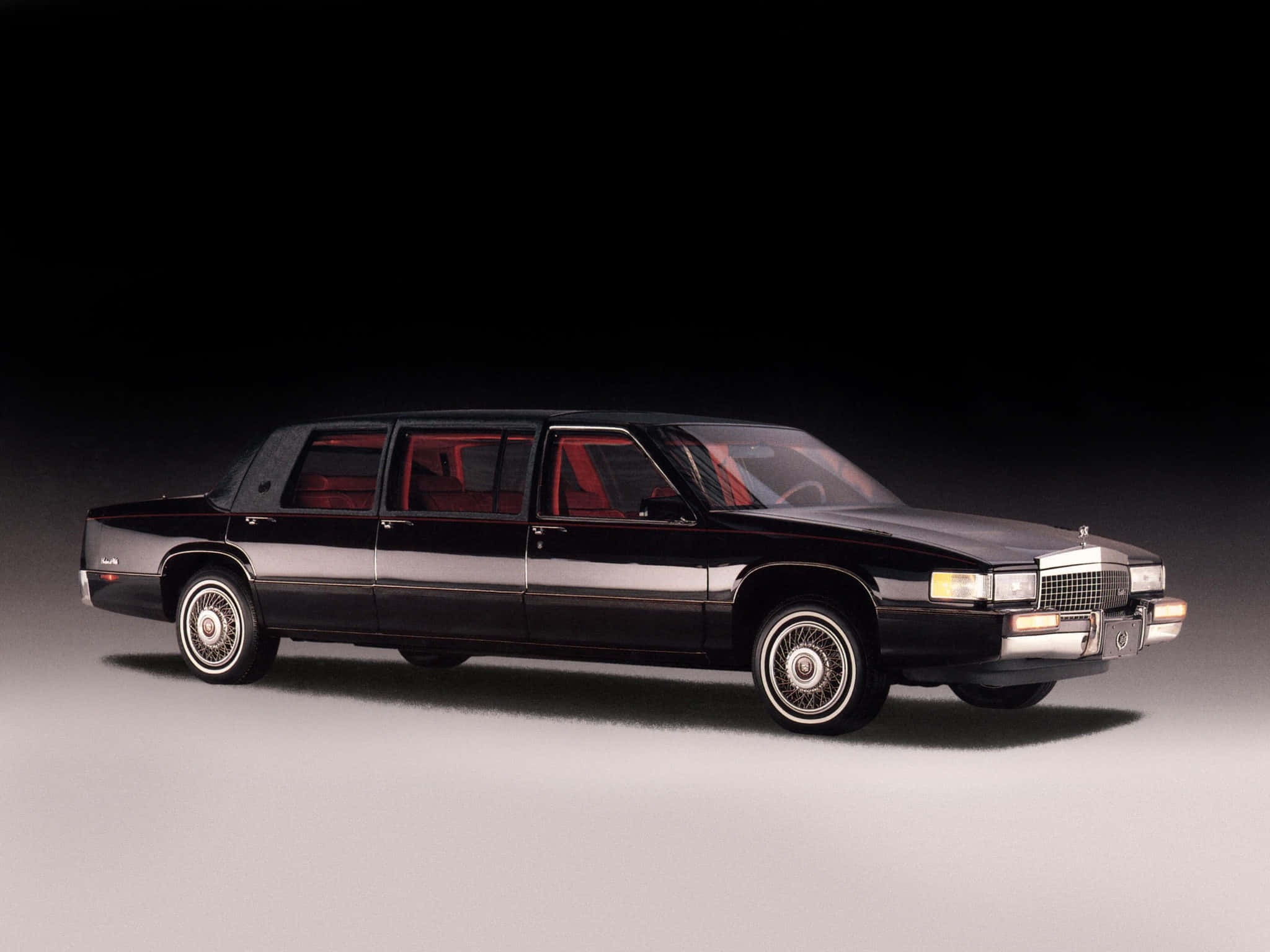 Cadillac Deville 桌布 壁紙 — 一輛時尚黑色豪華轎車搭配紅色內飾，在深色漸層背景前展現奢華與力量。