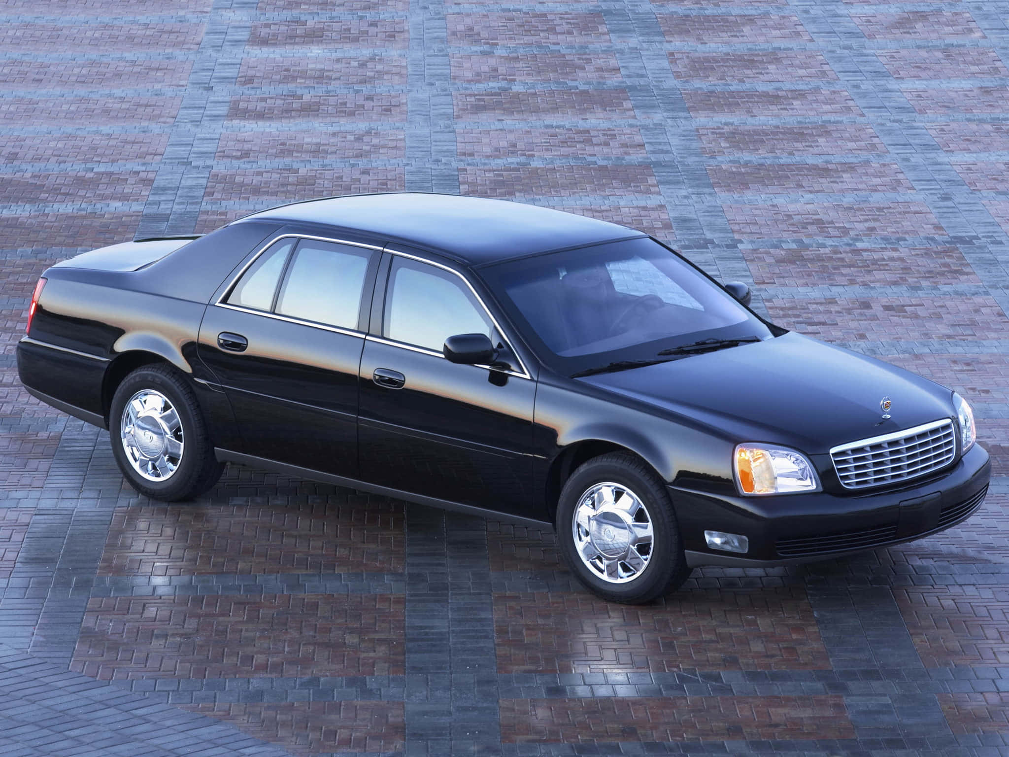 Cadillac Deville 桌布 壁紙 — 一輛時尚黑色豪華轎車停放在圖案磚砌廣場上，在明亮的日光下。