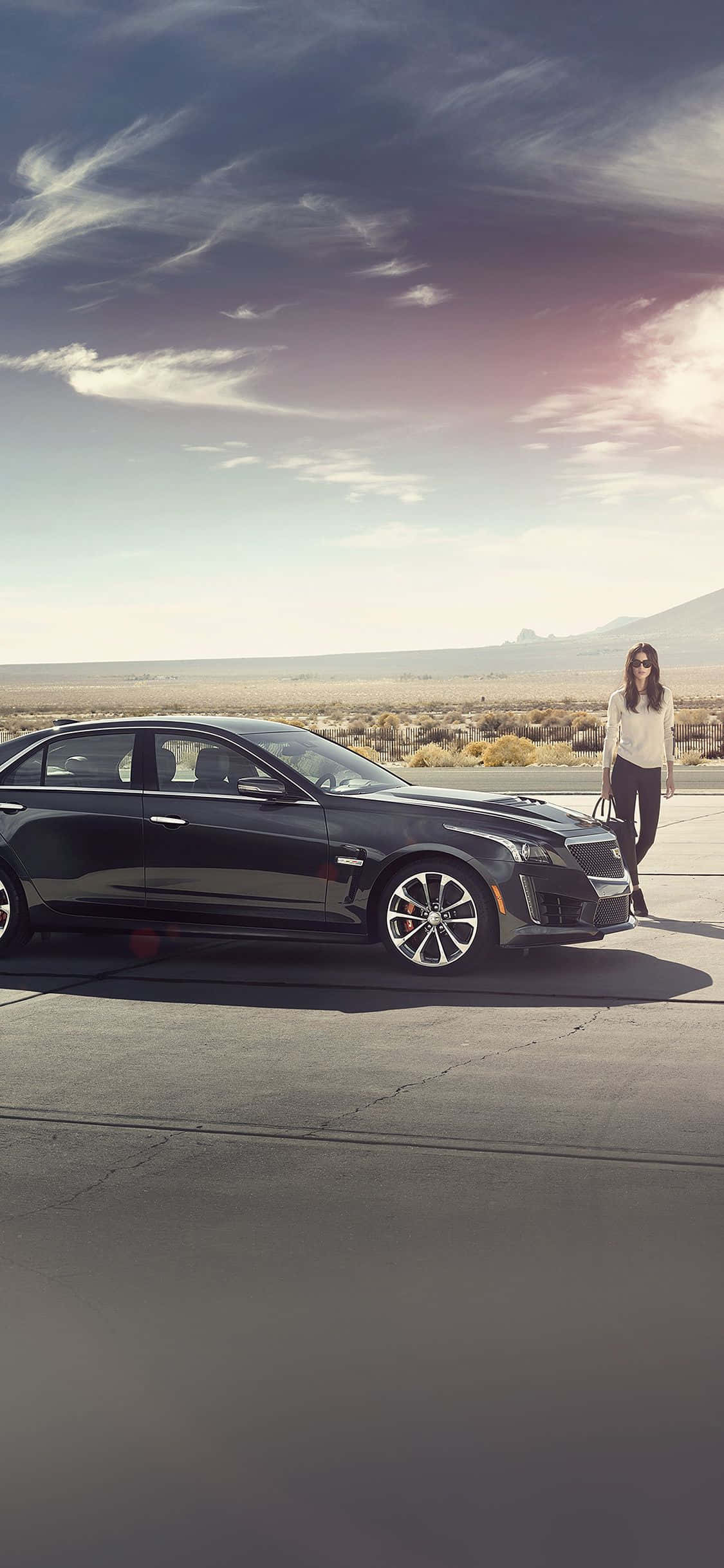 Cadillac Cts 桌布 壁紙 — 一輛時尚黑色豪華轎車停在沙漠公路上，一名女子站在車旁，背景是戲劇性的暮色天空。