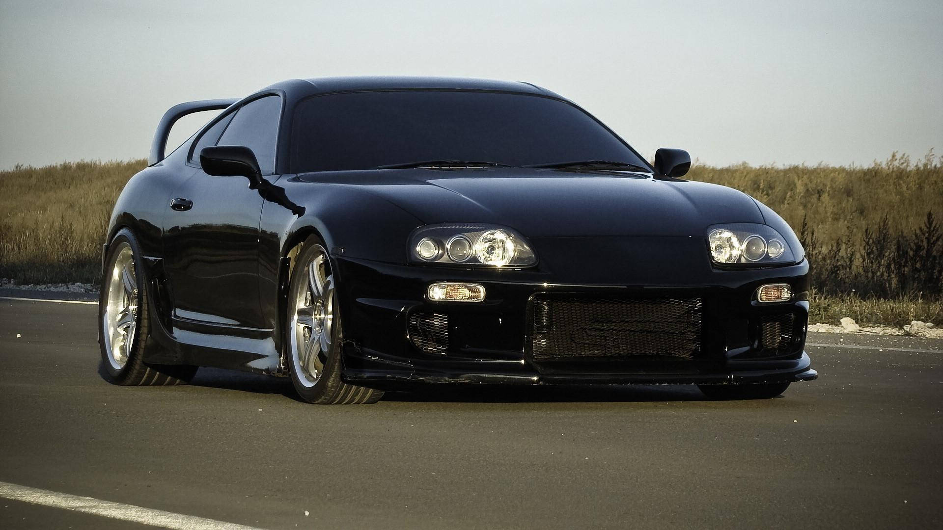 黑色跑車配備客製化輪圈，黃昏時停放在路邊。 — Toyota Supra 壁紙