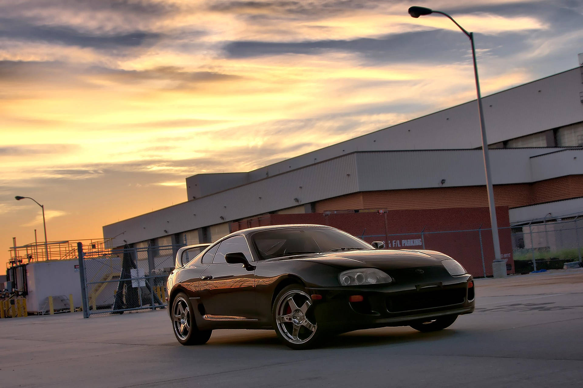 黑色跑車停放在工業用地，金色夕陽下。 — Toyota Supra 壁紙