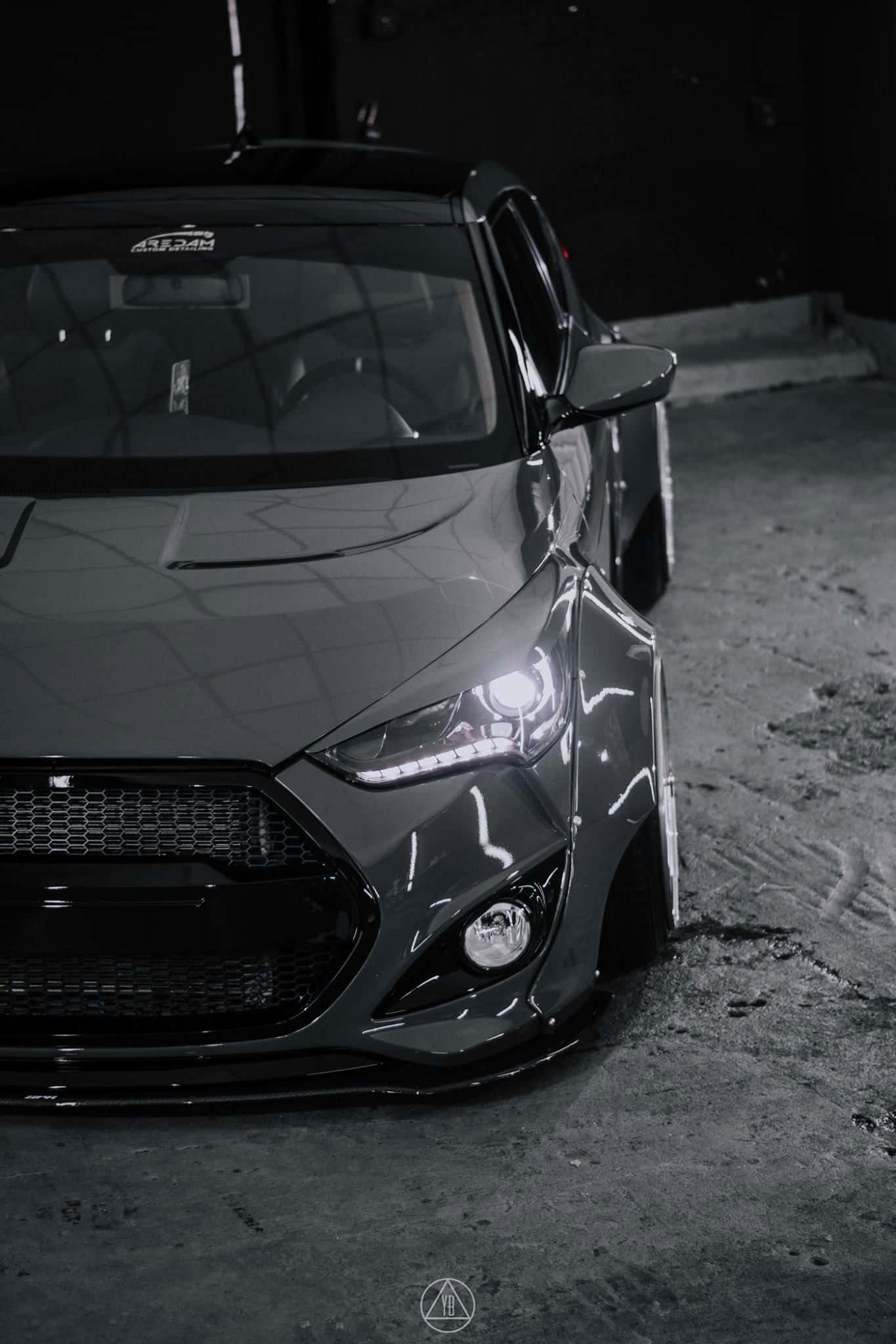 Hyundai Veloster 桌布 壁紙 — 一輛時尚灰色改裝車，車頭燈發光，停在光線昏暗的混凝土車庫中。