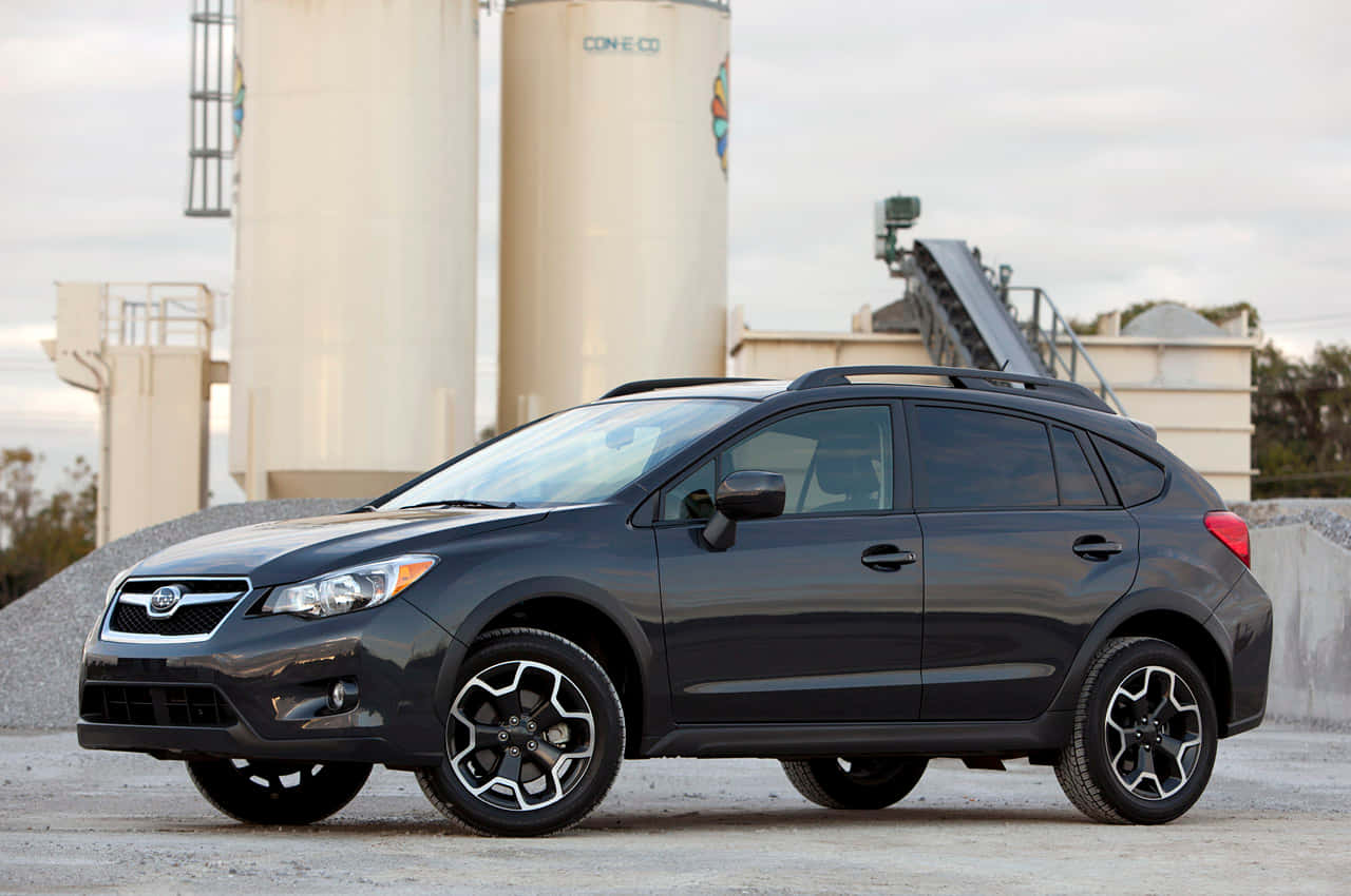 Fiat Tipo 桌布 壁紙 — 一輛時尚深灰色 Subaru Crosstrek SUV 停泊在碎石上，靠近大型工業筒倉，天空多雲。