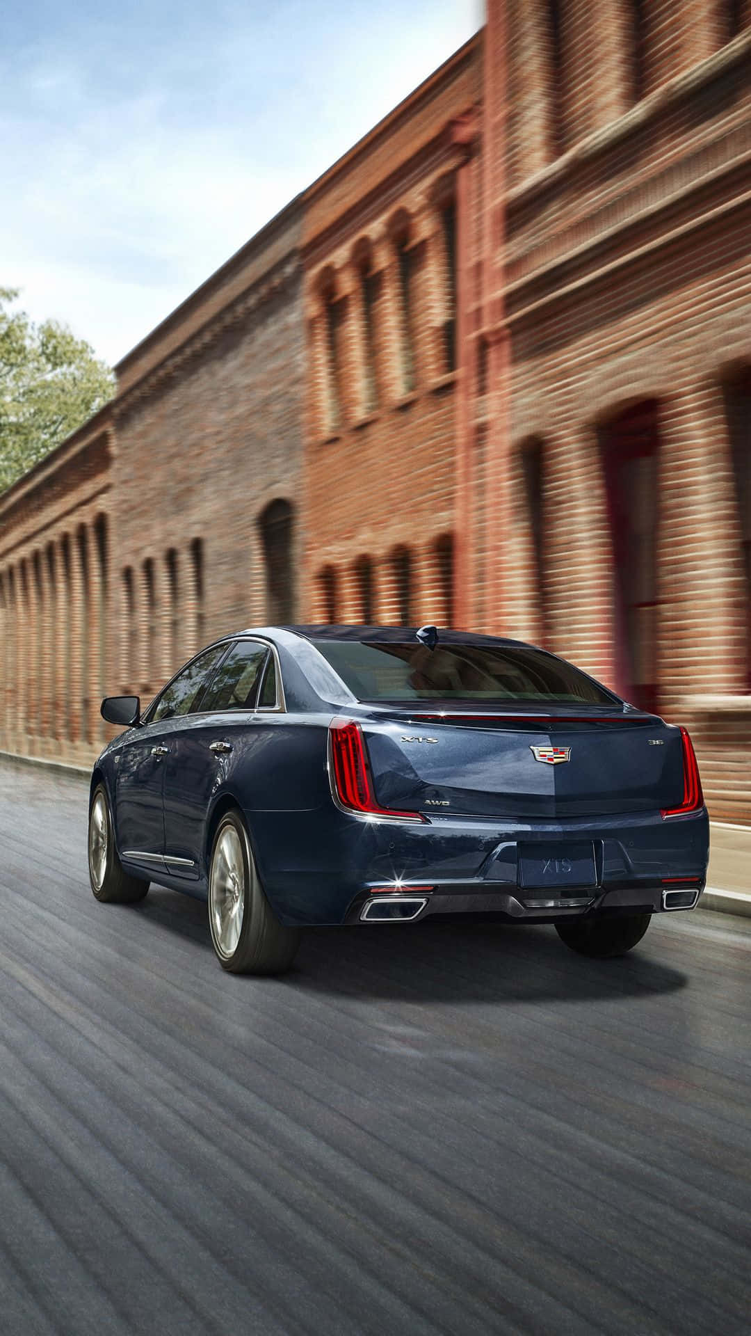 Cadillac Xts 桌布 壁紙 — 一輛時尚深藍色的Cadillac CT6在街上高速駛過紅磚建築，帶有動態模糊效果。