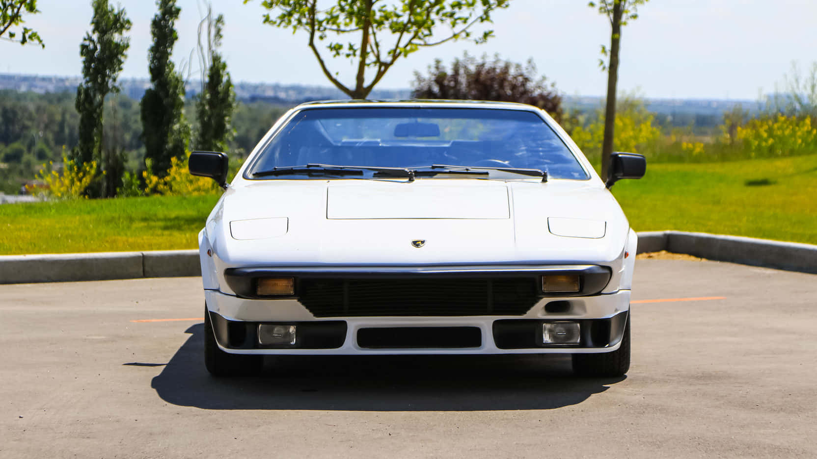 Lamborghini Silhouette 桌布 壁紙 — 一輛完美的白色藍寶堅尼Countach停放在陽光普照的混凝土停車場，背景有綠草和樹木。