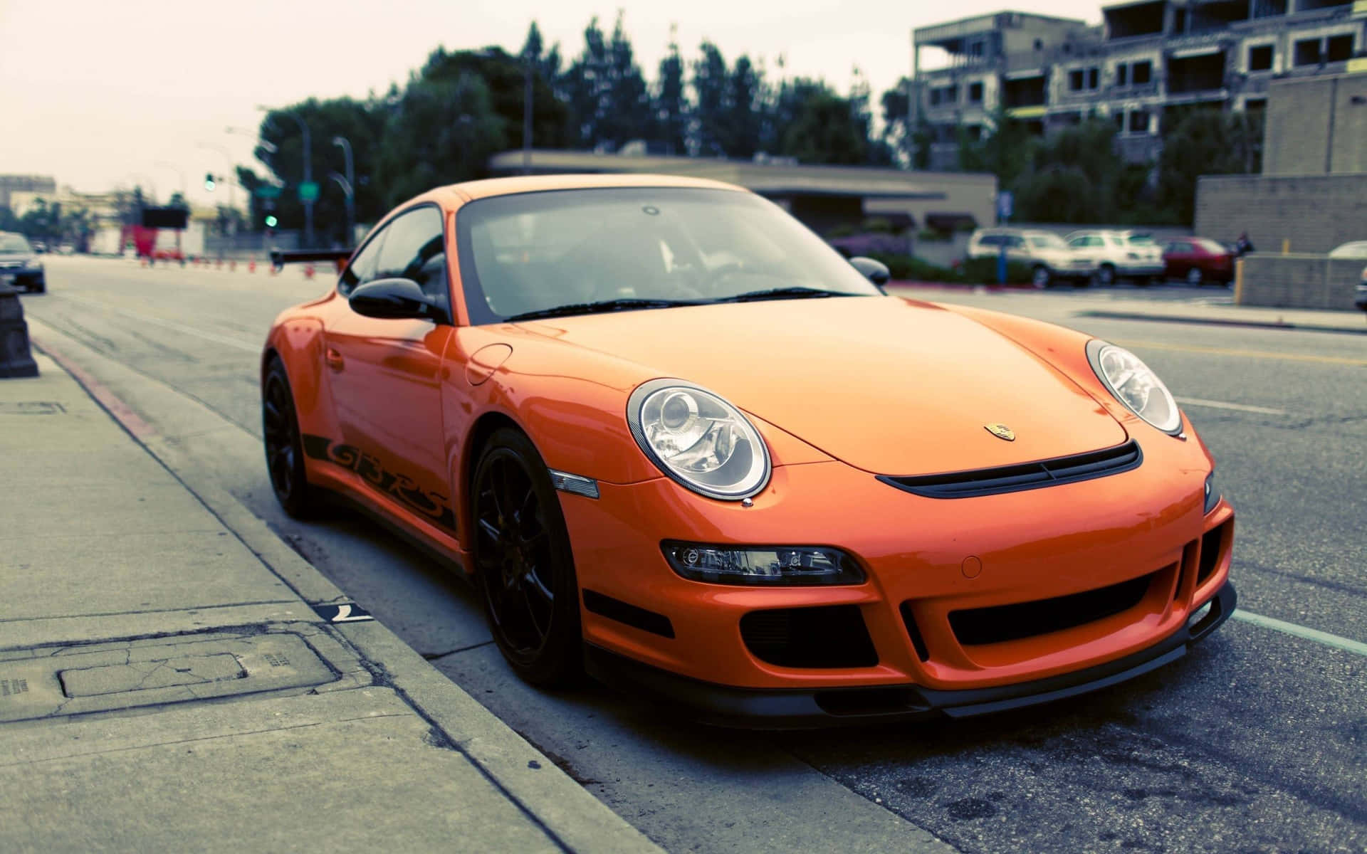  壁紙 — 一輛鮮橙色的保時捷911 GT3 RS停放在模糊城市背景的街道上。