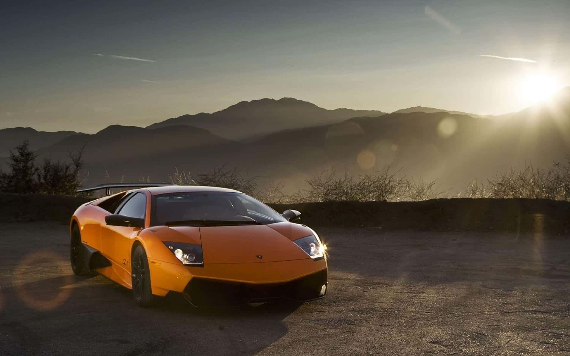 Lamborghini Murciélago 桌布 壁紙 — 一輛鮮橙色的藍寶堅尼 Murciélago 停泊在山路上，夕陽西下，鏡頭眩光，遠山連綿。
