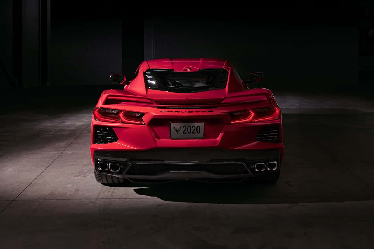  壁紙 — 一輛鮮紅色的2020年Corvette跑車在黑暗的混凝土車庫中從後方被戲劇性地照亮。