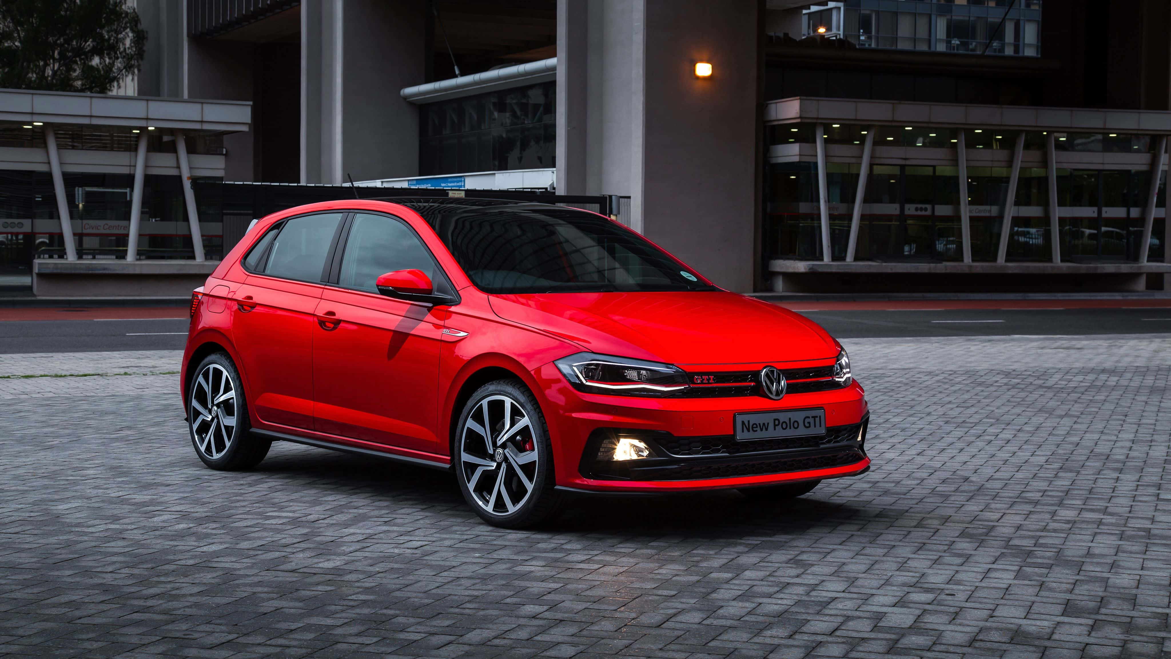 Volkswagen Polo 桌布 壁紙 — 一輛鮮紅色的福斯Polo GTI停放在鋪砌的都市廣場上，背景是現代建築。