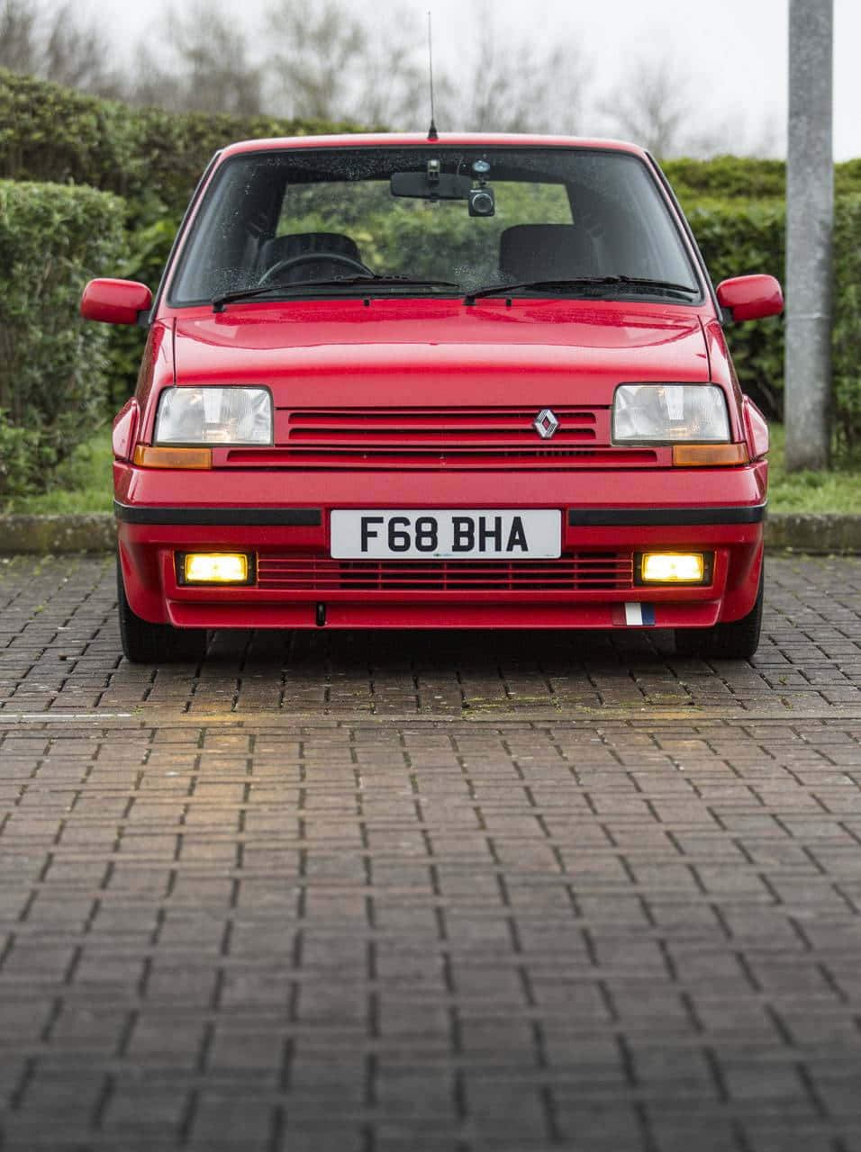 Renault 5 Turbo 桌布 壁紙 — 一輛鮮紅色的經典雷諾5 Turbo停泊在潮濕的磚砌車道上，背景有綠色樹籬。