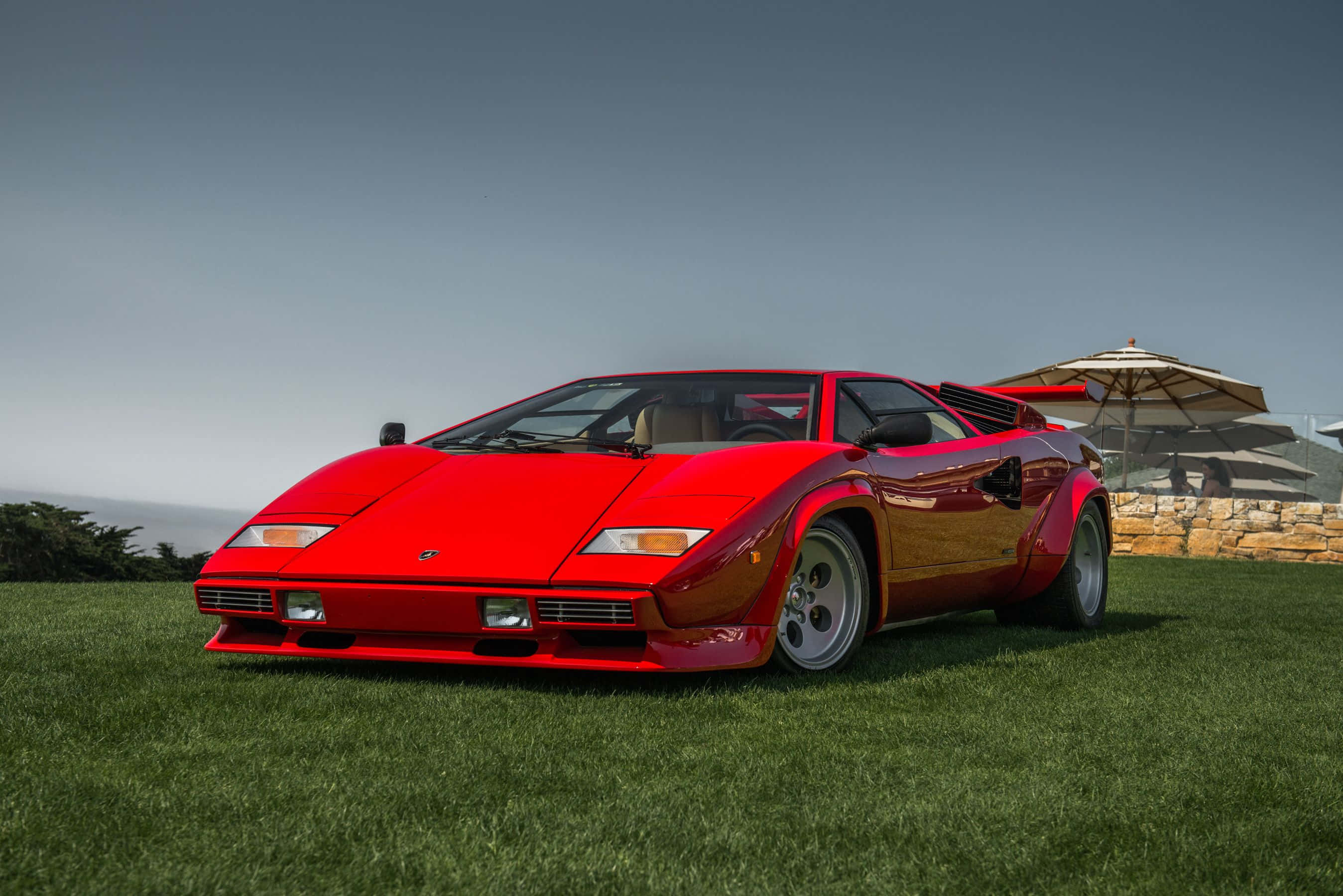 Lamborghini Countach 桌布 壁紙 — 一輛鮮紅色的藍寶堅尼Countach停放在茂盛的綠草地上，背景有海景和石牆。