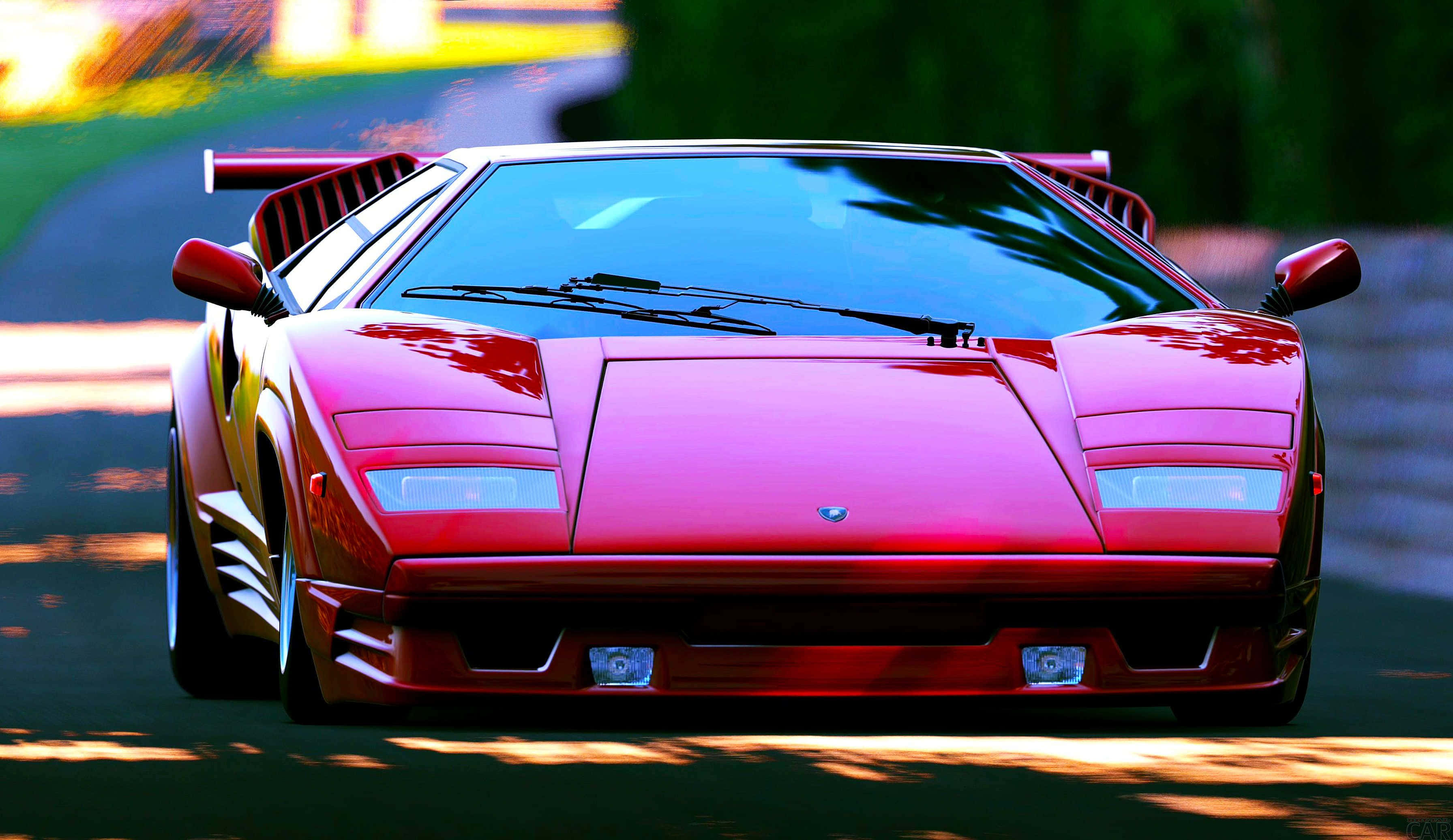 Lamborghini Countach 桌布 壁紙 — 一輛鮮紅色的藍寶堅尼Countach在陽光明媚的道路上行駛，背景是模糊的綠色植物。