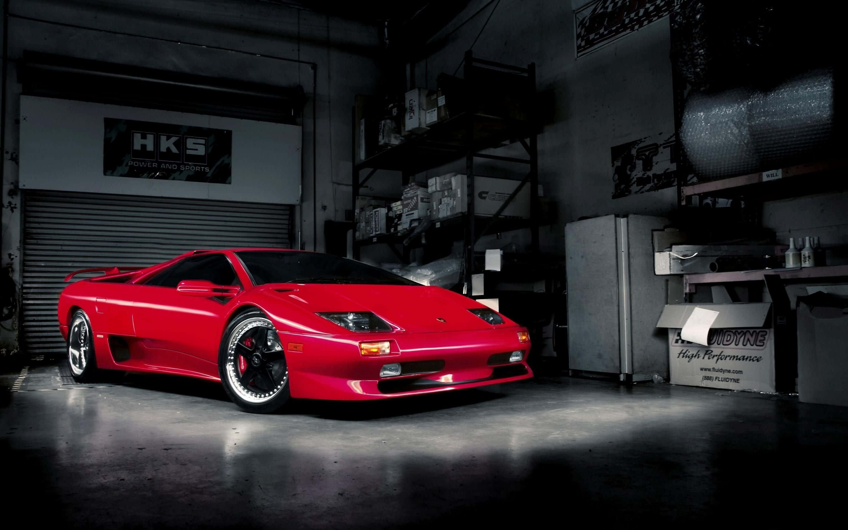 Lamborghini Diablo 桌布 壁紙 — 一輛鮮紅色的藍寶堅尼Diablo跑車在雜亂的工業車庫中，在戲劇性的聚光燈下閃閃發光。