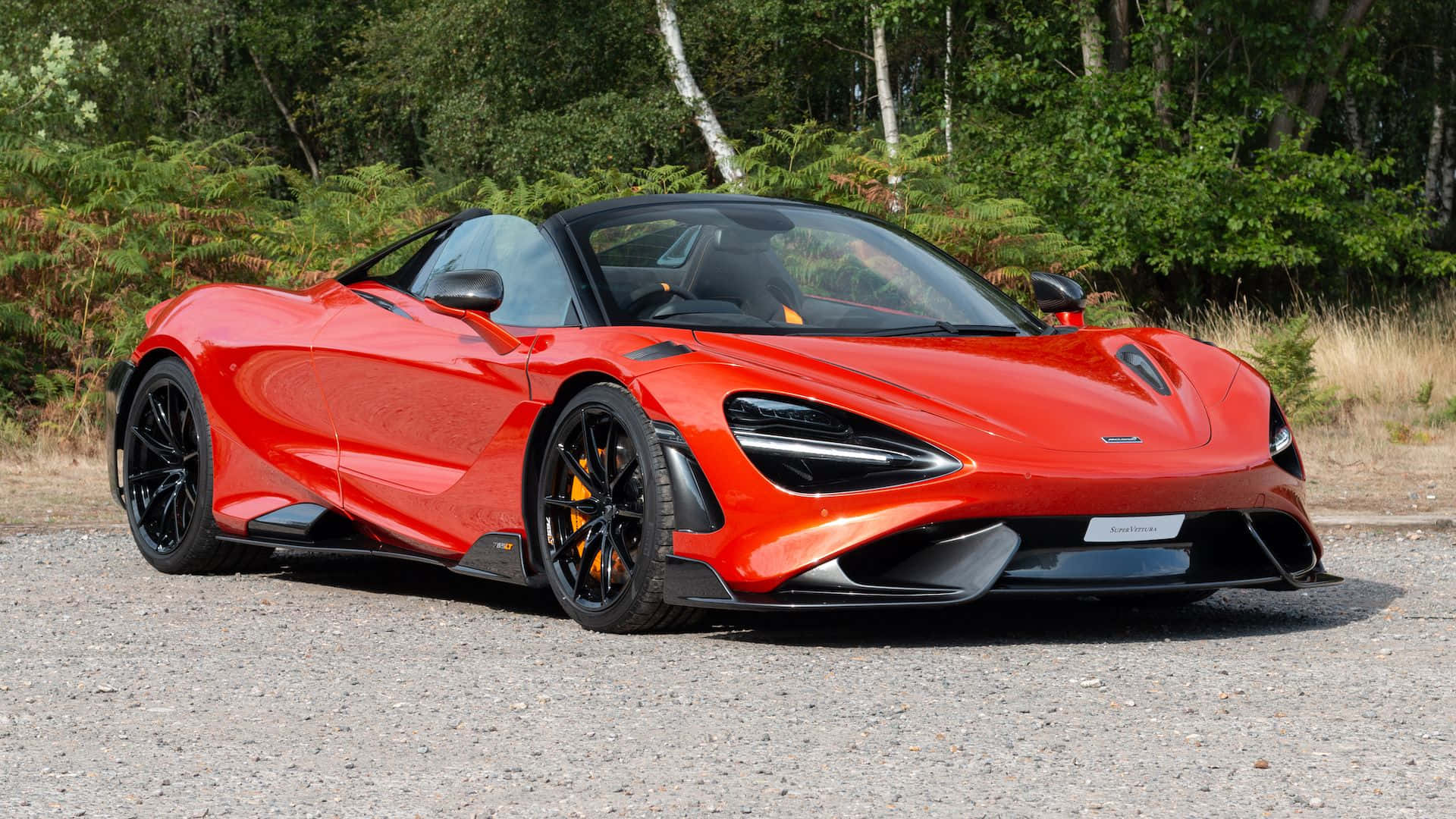 Mclaren 765lt 桌布 壁紙 — 一輛鮮紅色的McLaren 720S Spider停在碎石上，背景是茂密的綠色森林。