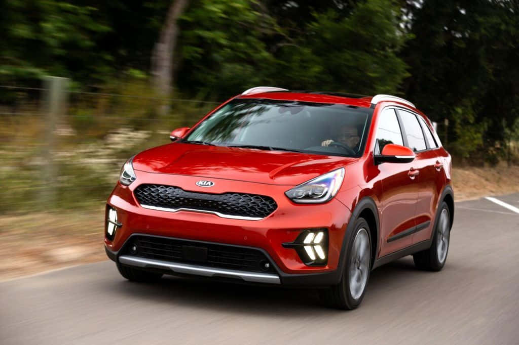 Kia Niro 桌布 壁紙 — 一輛鮮紅色的起亞Niva SUV沿著蜿蜒的道路疾馳，茂密的綠樹在運動中模糊。