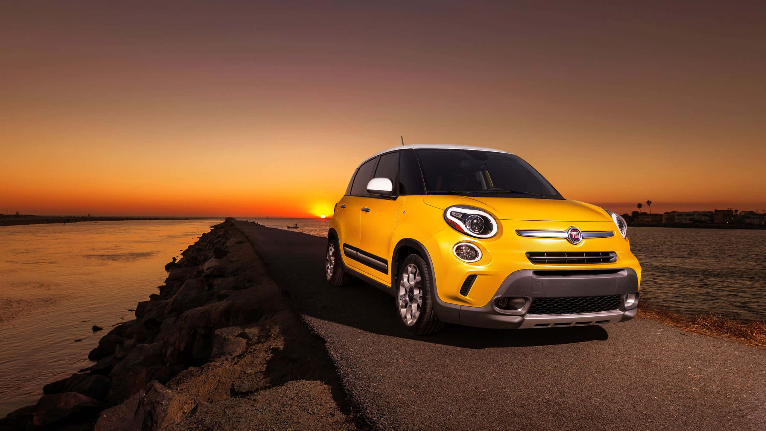 Fiat 500l 桌布 壁紙 — 一輛鮮黃色的Fiat 500L在日落時分停泊在沿海公路上，天空呈現溫暖的橙色和紫色。