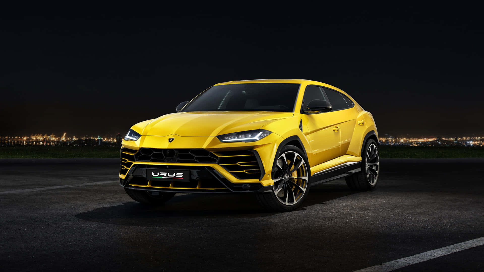 黃色藍寶堅尼 Urus SUV 夜間停泊，背景有城市燈光。 — 蘭博基尼 壁紙