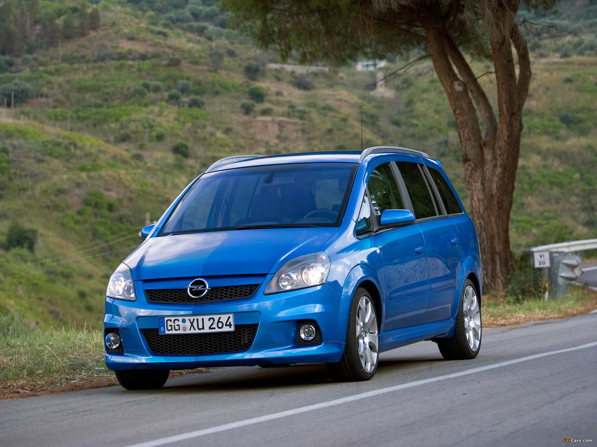 Opel Zafira 桌布 壁紙 — 一輛鮮藍色的歐寶Zafira沿著蜿蜒的鄉村道路行駛，兩旁是綠色的山丘和一棵大樹。