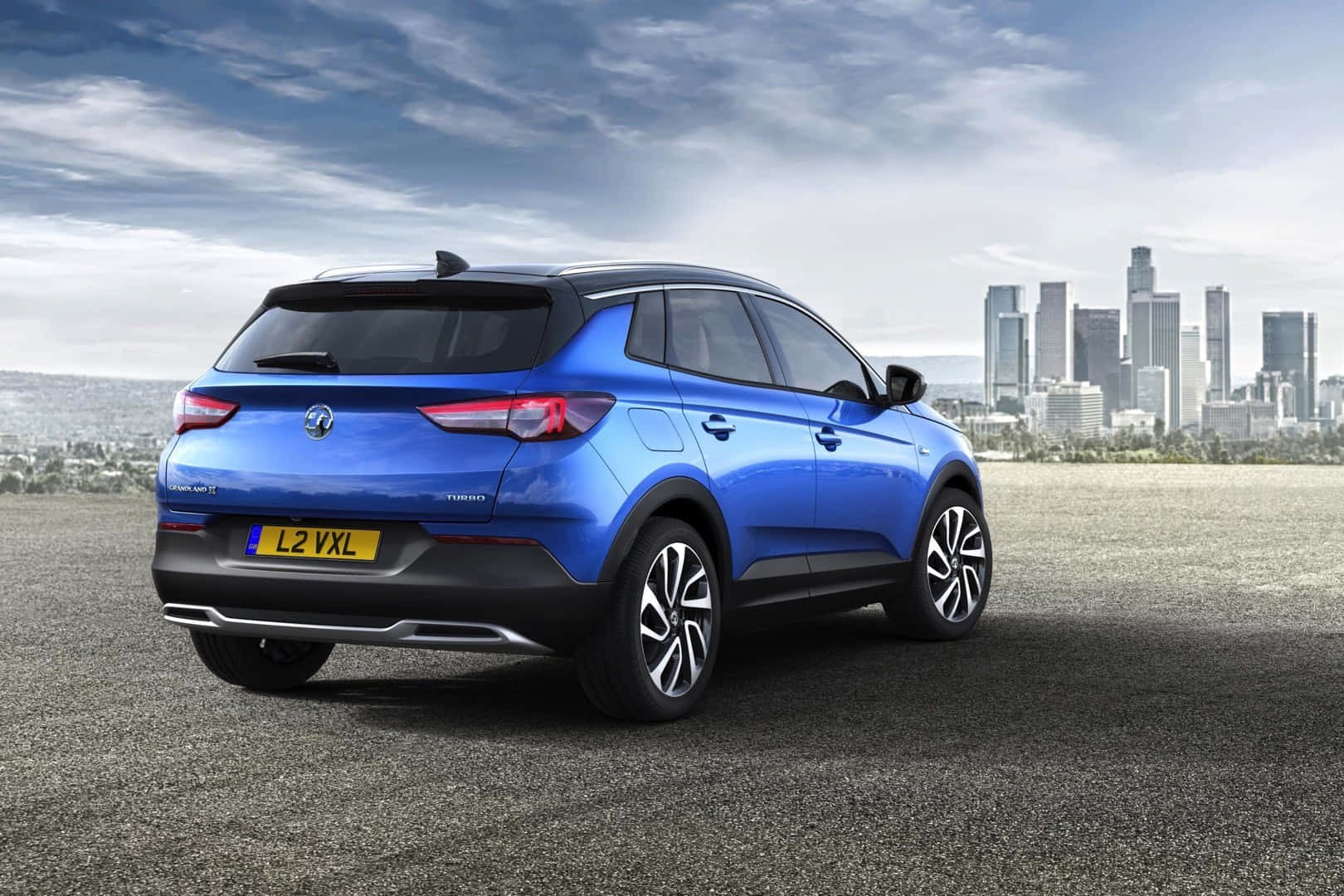 Opel Grandland X 桌布 壁紙 — 一輛鮮藍色的Vauxhall Crossland X SUV停在瀝青路上，背景是現代城市天際線，天空多雲。