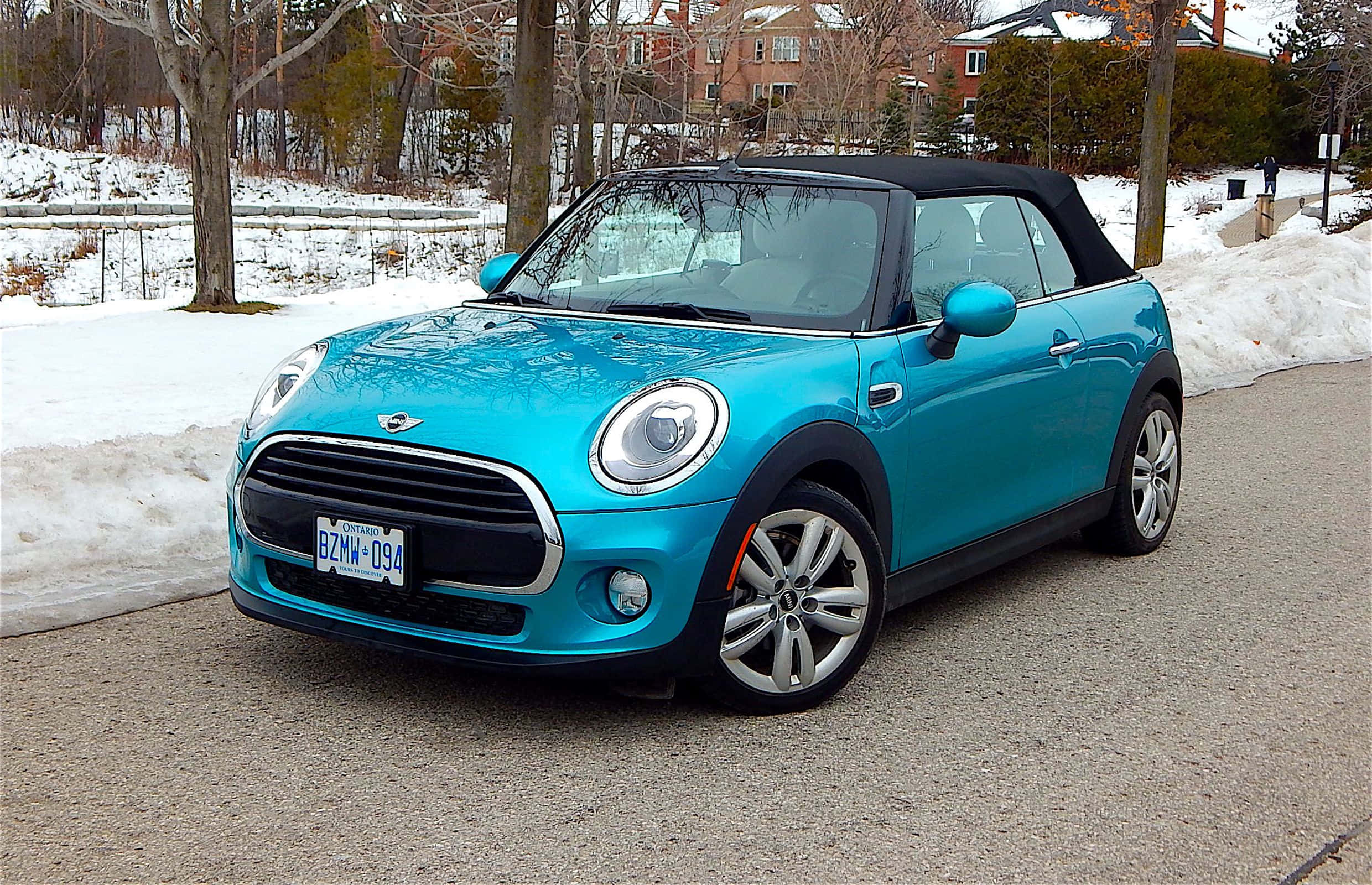Mini Cooper Convertible 桌布 壁紙 — 一輛鮮豔的綠松色MINI Cooper敞篷車停泊在積雪的路邊，背景有光禿的樹木和磚屋。