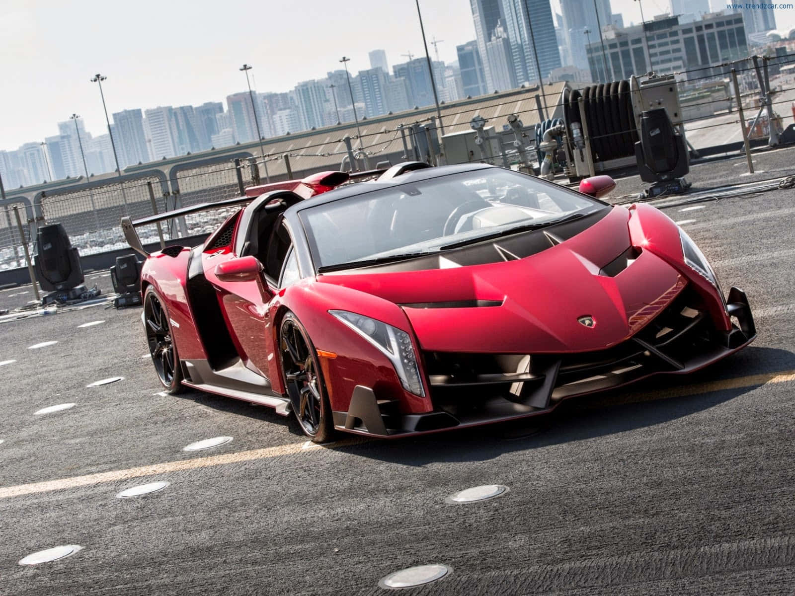 Lamborghini Veneno 桌布 壁紙 — 一輛醒目的紅色藍寶堅尼 Veneno Roadster 停泊在屋頂上，背景是現代化的城市天際線。