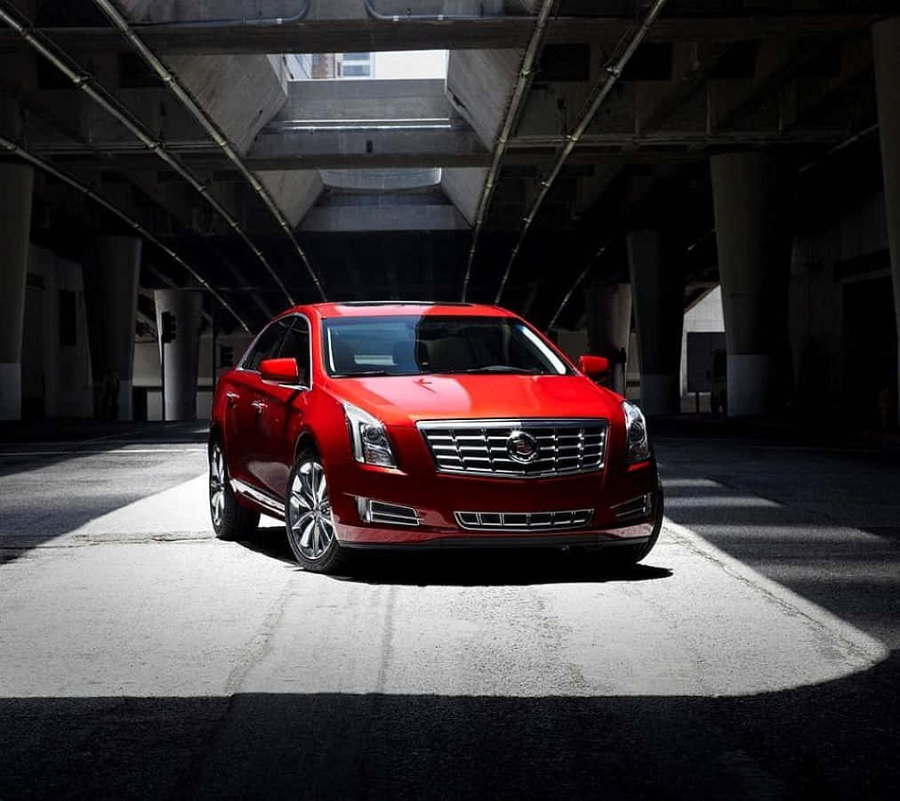 Cadillac Xts 桌布 壁紙 — 一輛引人注目的紅色凱迪拉克轎車在陰暗的混凝土停車場中，在一束陽光下閃閃發光。