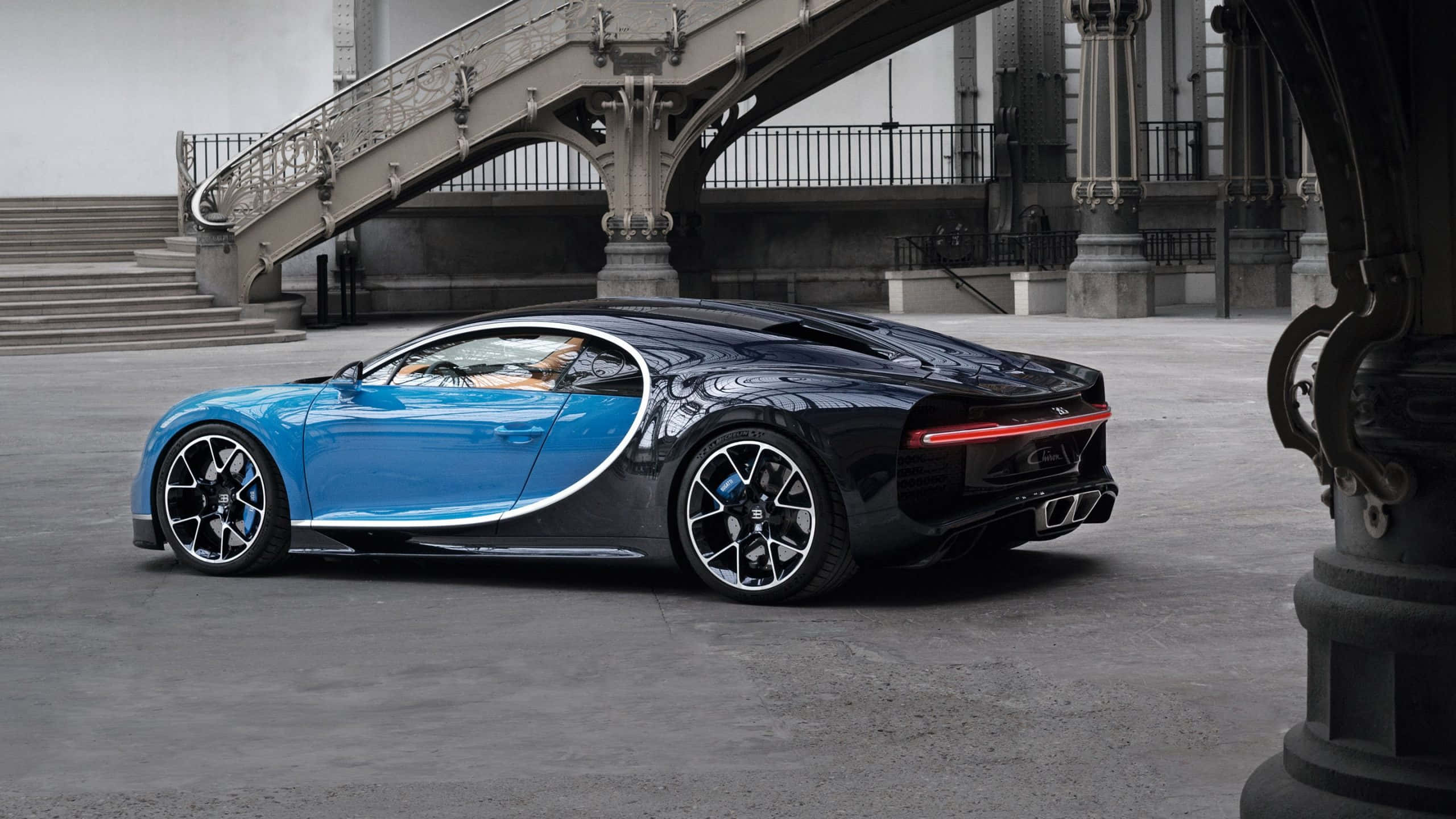 Bugatti Chiron 桌布 壁紙 — 一輛引人注目的藍黑布加迪Chiron停在裝飾華麗的石橋下，橋上有精緻的欄杆和柱子。
