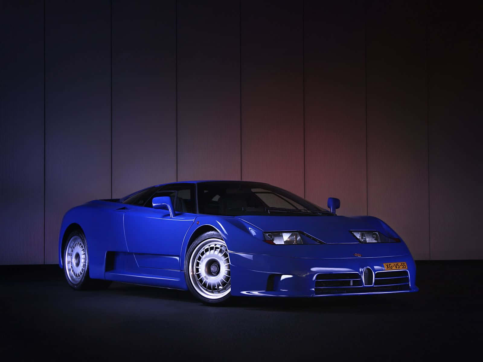 Bugatti Eb110 桌布 壁紙 — 一輛引人注目的藍色Bugatti EB110超級跑車在戲劇性的攝影棚燈光下，在深色鑲板牆前閃閃發光。
