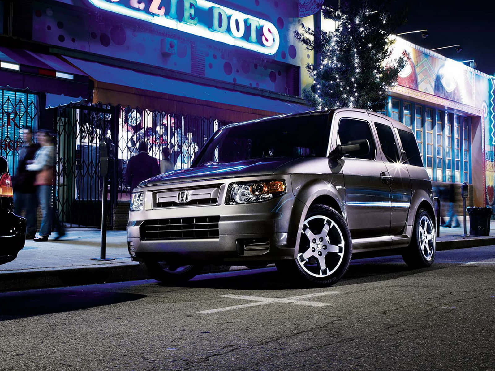 Honda Element 桌布 壁紙 — 一輛銀色本田Element停放在夜晚充滿活力的霓虹燈城市街道上，伴有節慶燈飾和行人。