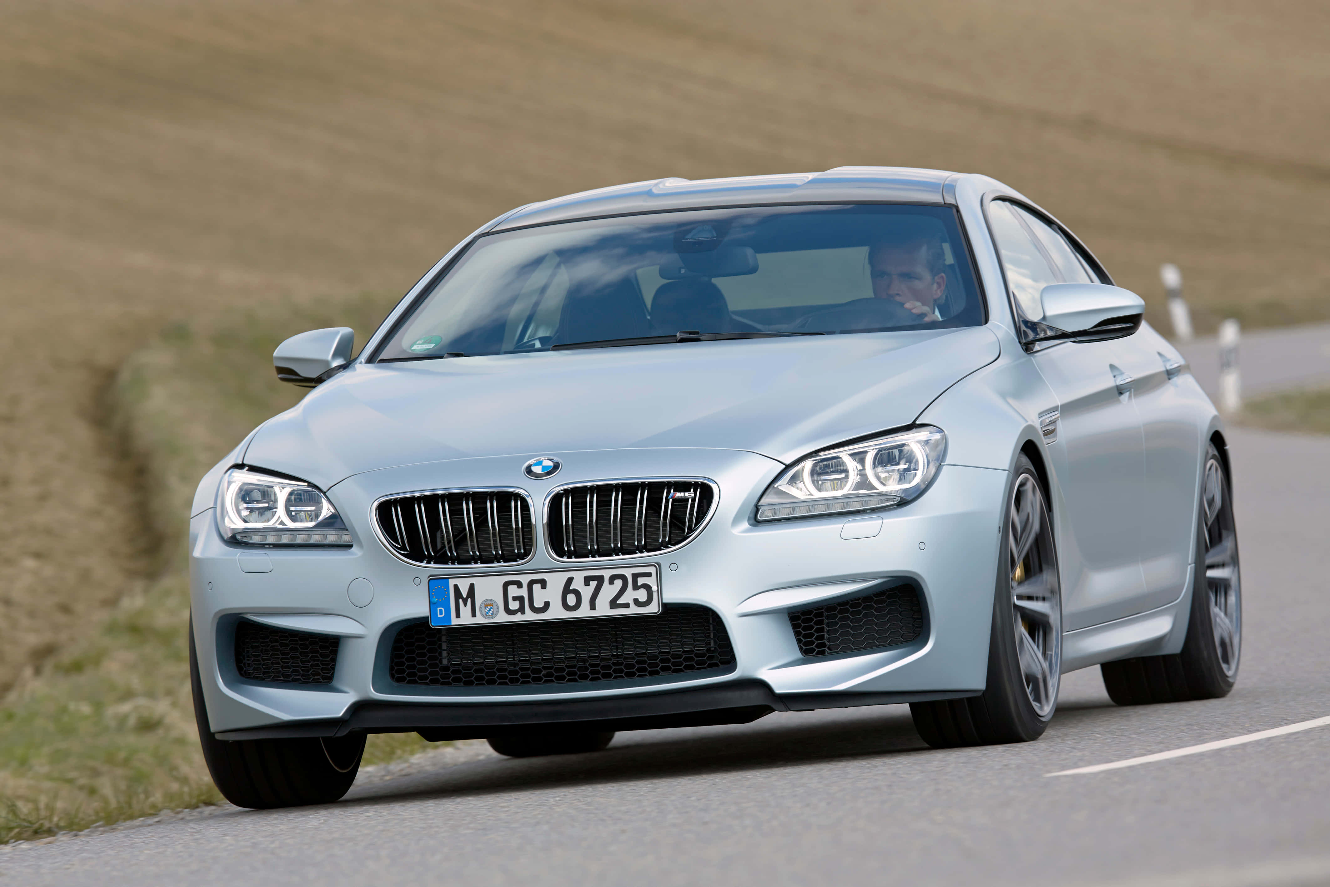 Bmw M6 桌布 壁紙 — 一輛銀色BMW M6雙門跑車在蜿蜒的鄉村道路上疾馳，駕駛透過擋風玻璃可見。