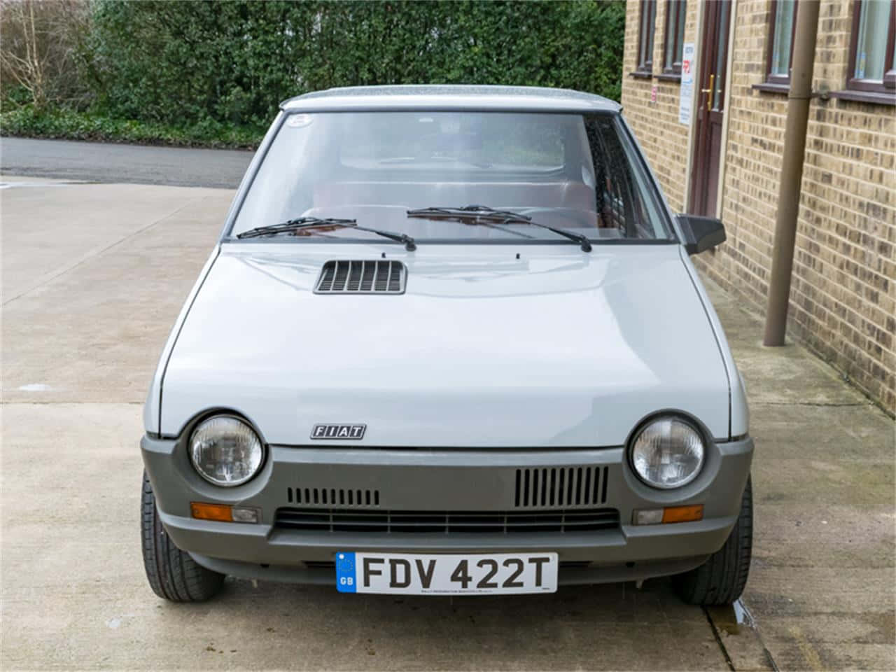 Fiat Ritmo 桌布 壁紙 — 一輛銀色的Fiat 126停在磚造建築旁的混凝土車道上，背景有綠色灌木。