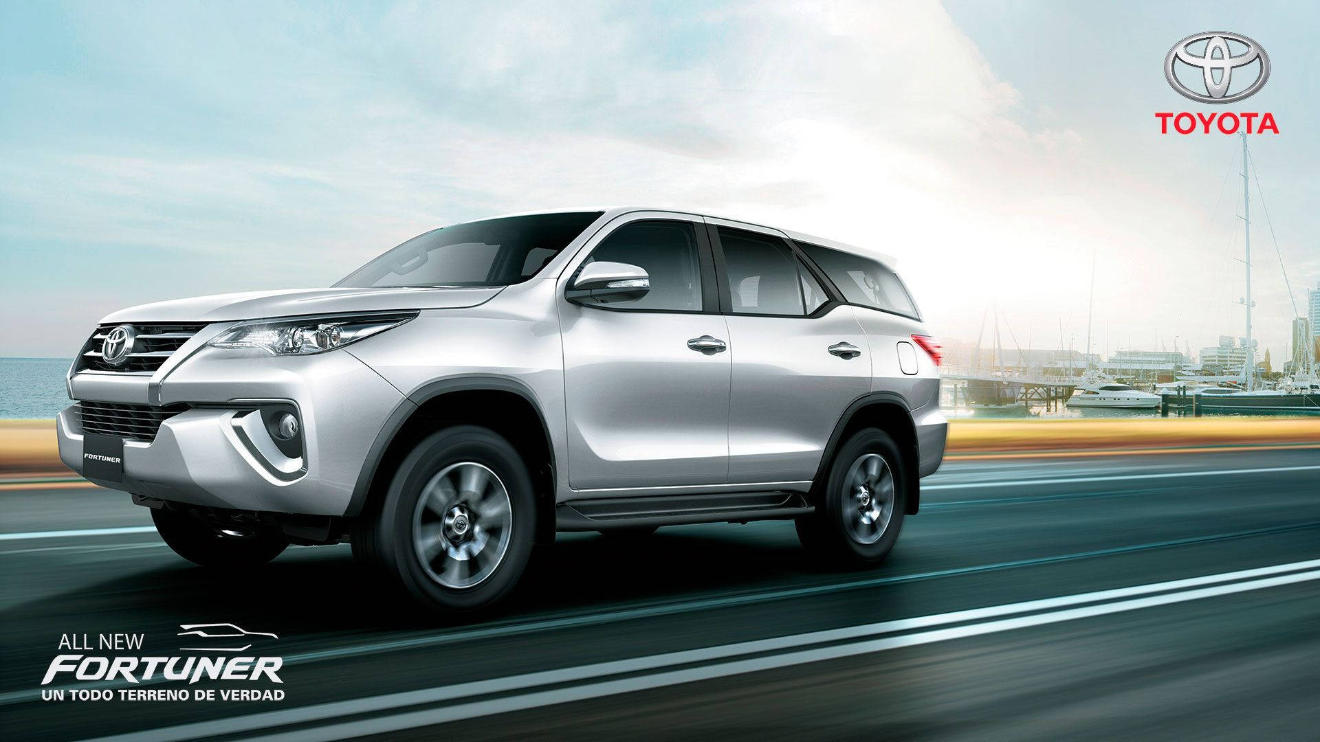 銀色豐田 Fortuner SUV 在碼頭附近的海岸道路上快速行駛。 — Toyota Supra 壁紙