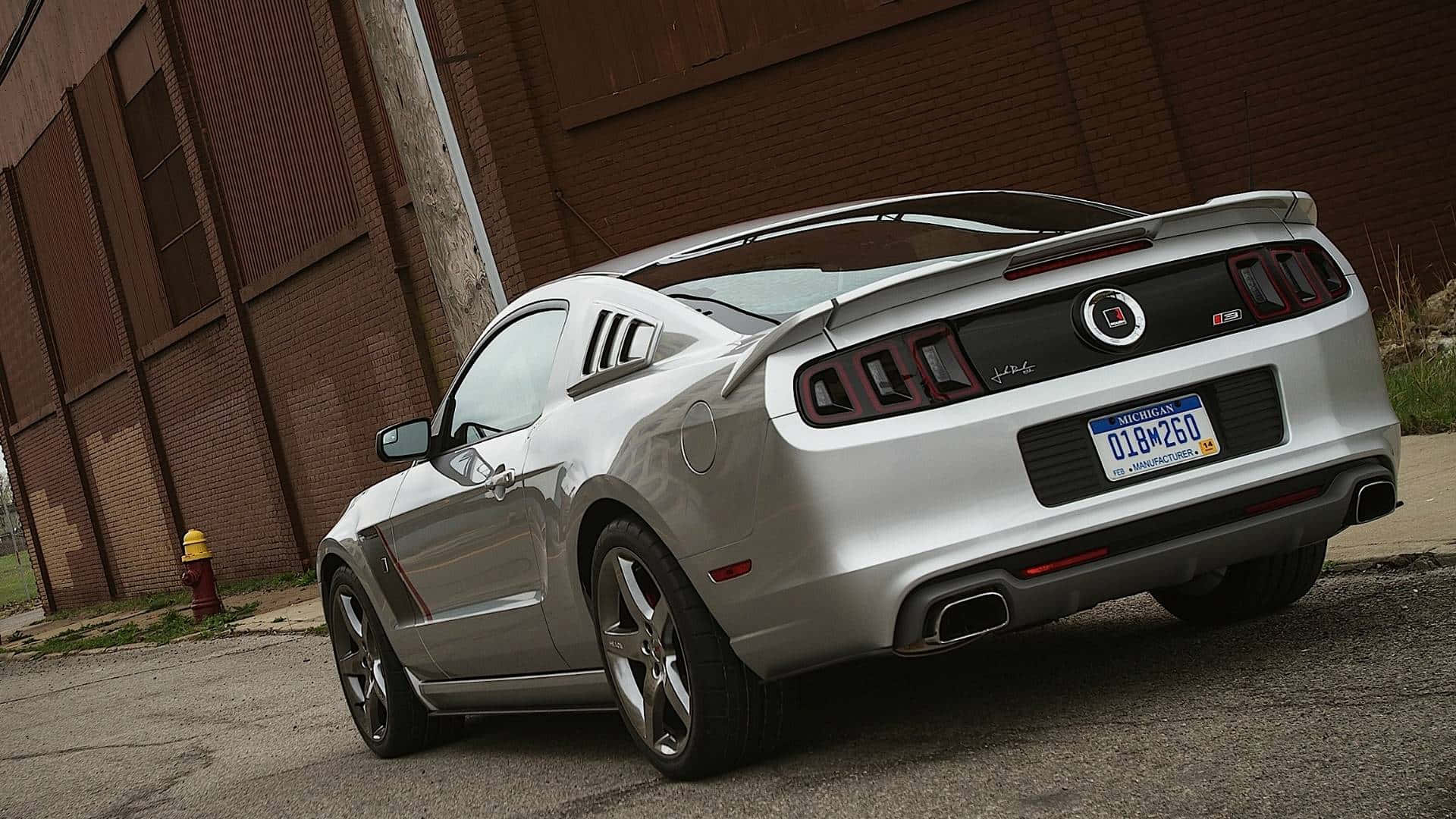 Ford Mustang Roush 桌布 壁紙 — 一輛銀色福特野馬GT斜停在磚造建築旁，附近有一個黃色消防栓。
