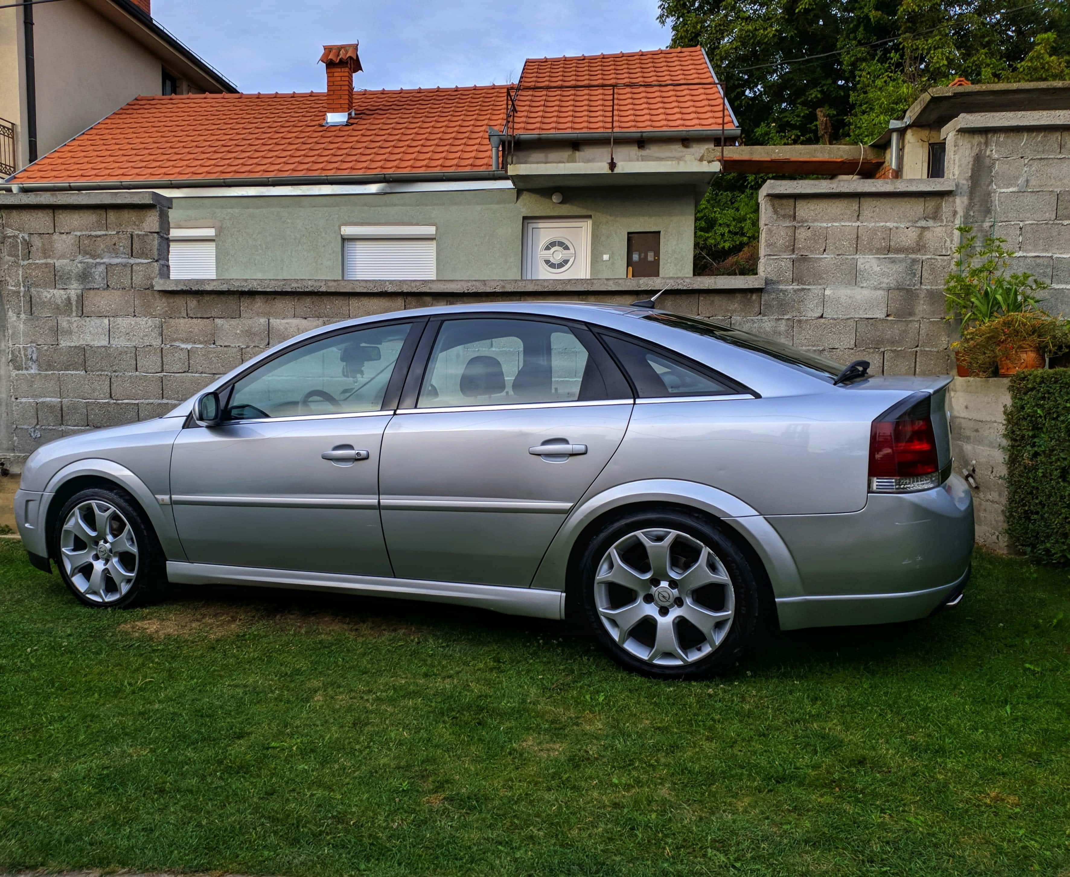 Opel Vectra 桌布 壁紙 — 一輛銀色轎車停放在石牆和瓦頂屋前的綠色草地上，天空多雲。