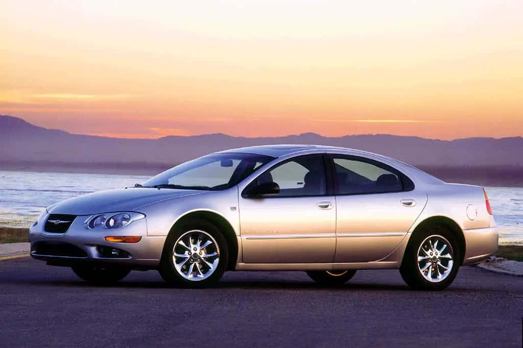 Chrysler Lhs 桌布 壁紙 — 一輛銀色轎車在日落時停泊在人行道上，背景有山和水。
