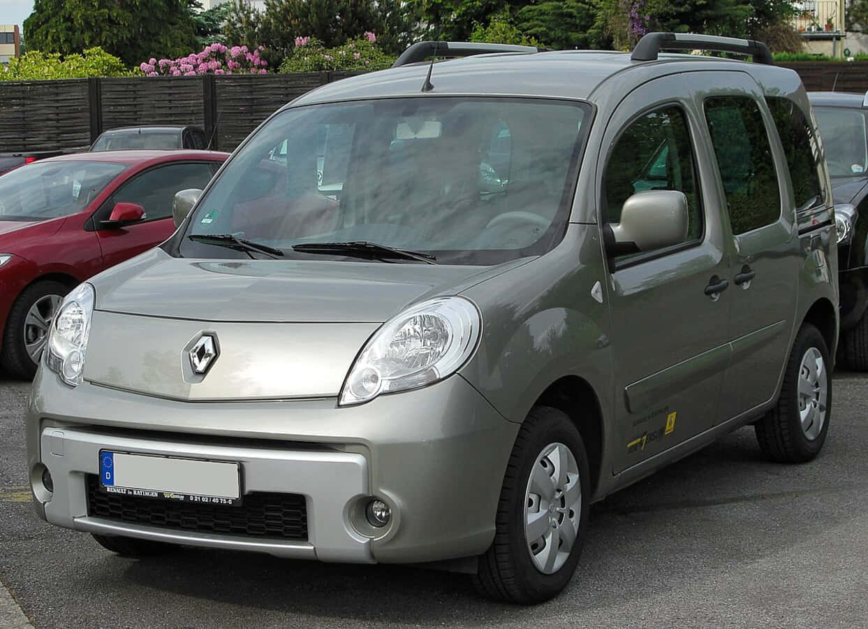 Renault Kangoo 桌布 壁紙 — 一輛銀色雷諾Kangoo客貨車停在一個有綠化和粉紅色花朵背景的停車場。