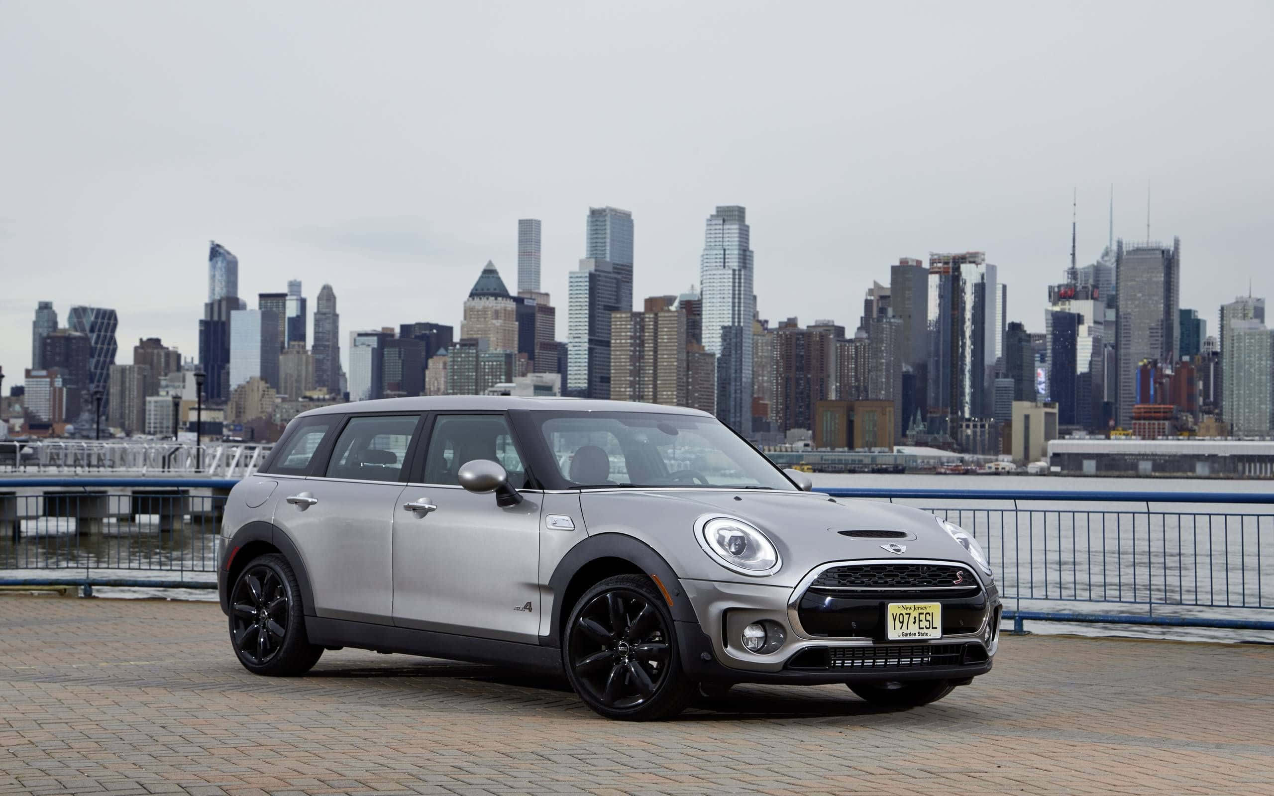 Mini Cooper S Clubman All4 桌布 壁紙 — 一輛銀色MINI Countryman停泊在磚砌海濱長廊上，背景是陰天的城市天際線。