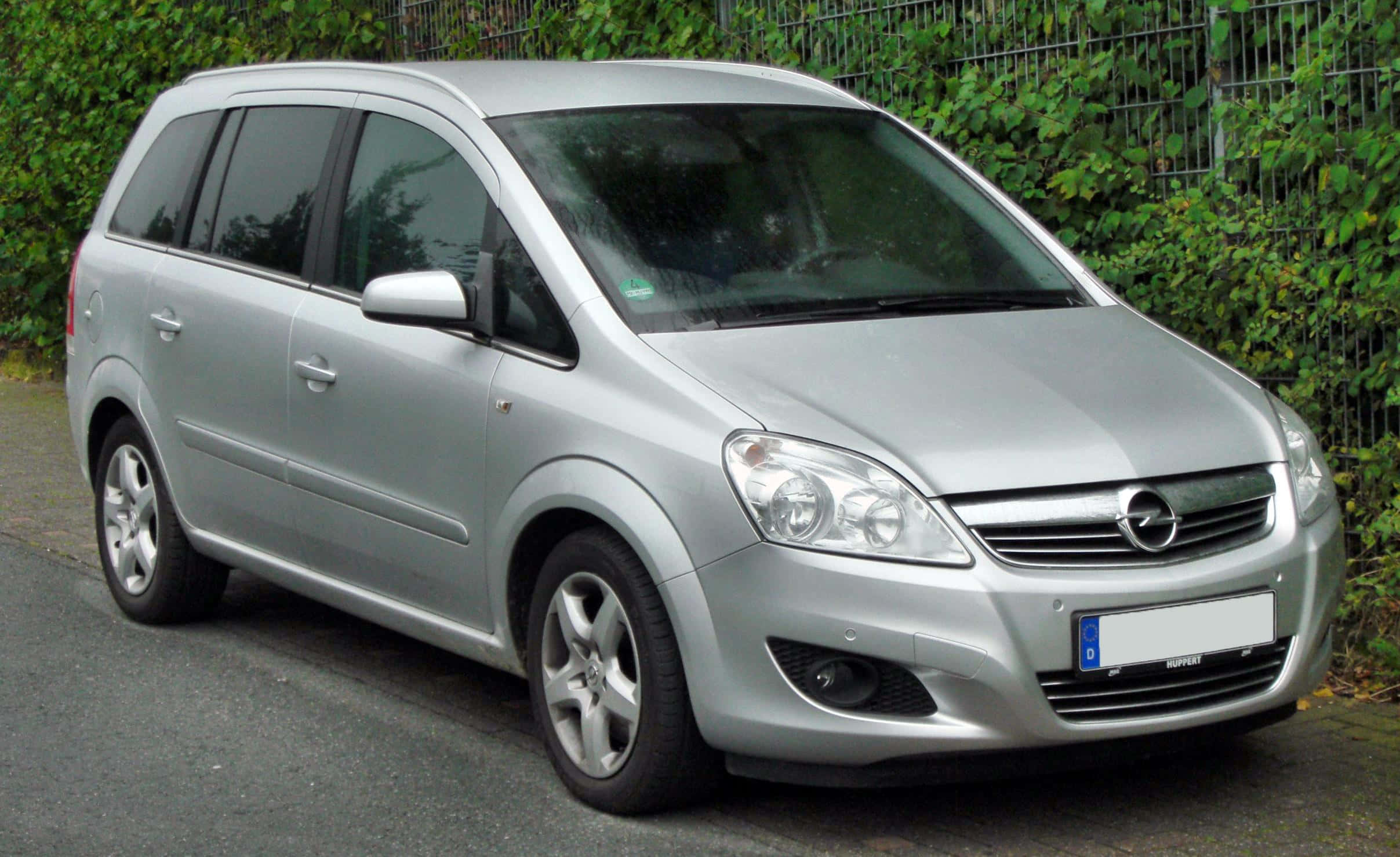 Opel Zafira 桌布 壁紙 — 一輛銀色歐寶Zafira小型貨車停在柏油路上，旁邊是綠色常春藤覆蓋的圍欄。