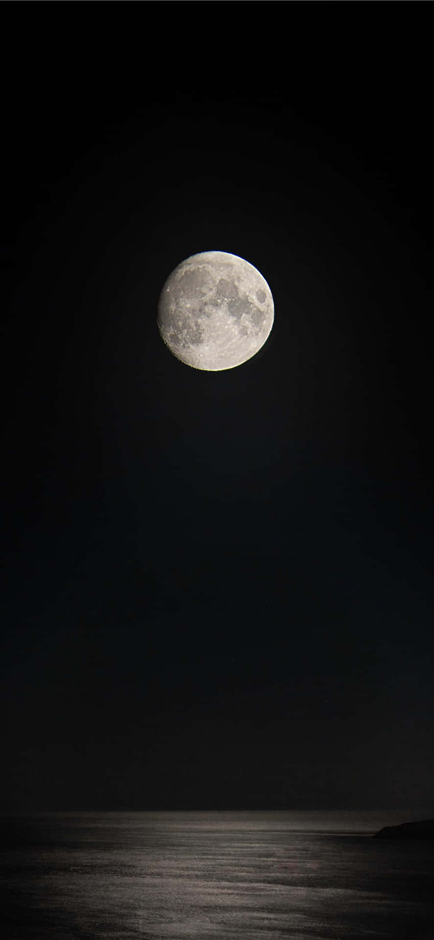 滿月映照在夜間平靜的海洋上，天空漆黑 — iPhone 11 壁紙