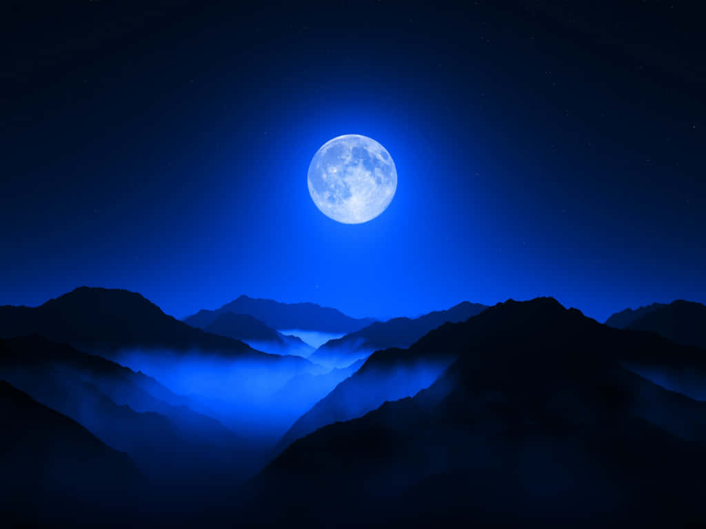  壁紙 — 一輪明亮的滿月在繁星點點的夜空下，將冷藍色的光芒投射在籠罩於霧谷中的剪影山峰上。