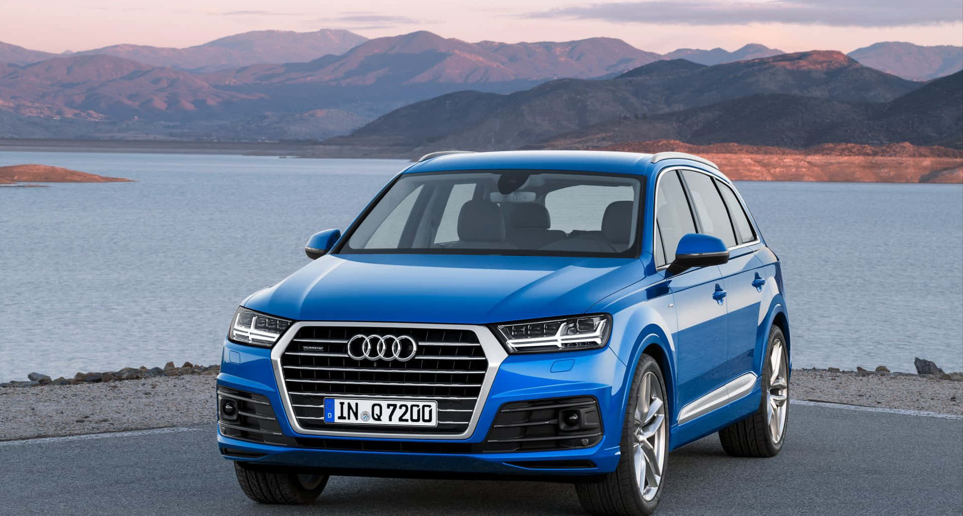 Audi Q7 桌布 壁紙 — 一輛充滿活力的藍色 Audi Q7 SUV 停泊在寧靜的湖邊，山脈在柔和的暮色中閃耀。