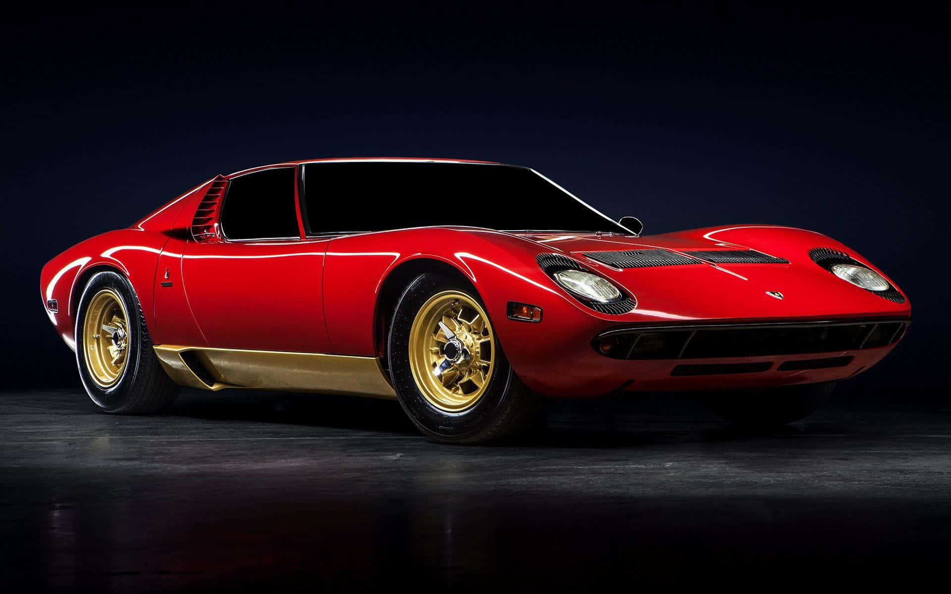 Lamborghini Miura 桌布 壁紙 — 一輛帶有金色飾邊和輪轂的亮紅色藍寶堅尼 Miura 在深色背景下的攝影棚燈光中閃耀。