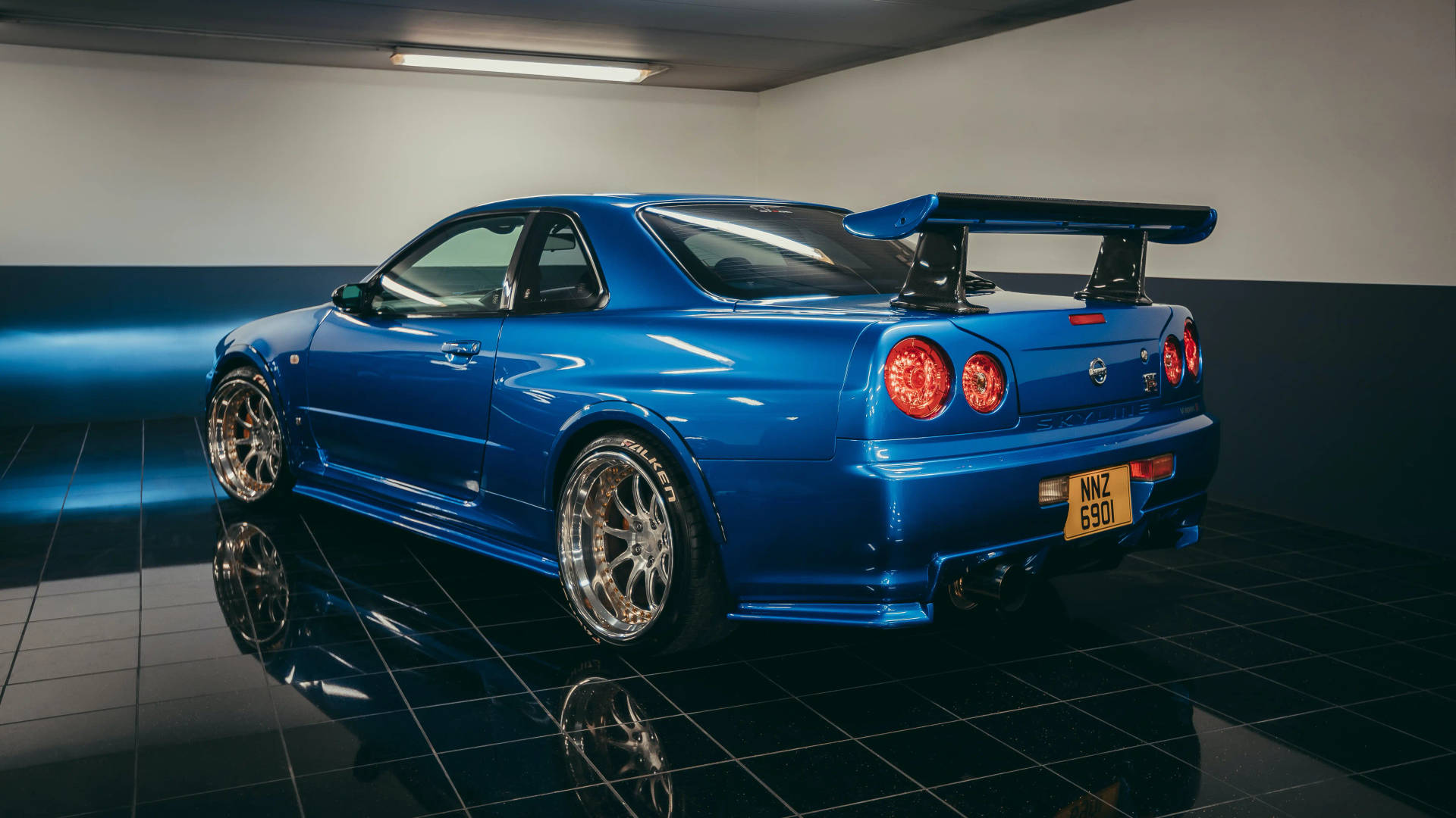 藍色日產Skyline R34跑車，帶後擾流板，在帶有反光的深色瓷磚車庫中。 — 天際線 壁紙